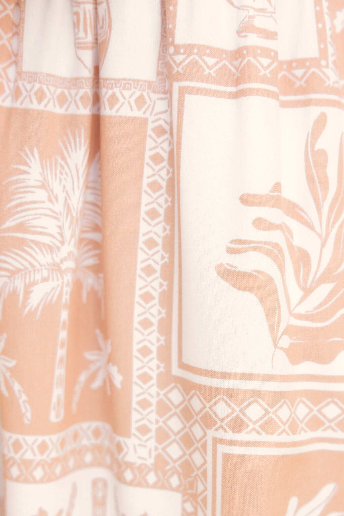Close-up of light coral fabric featuring palm and leaf prints, perfect for casual summer wear.