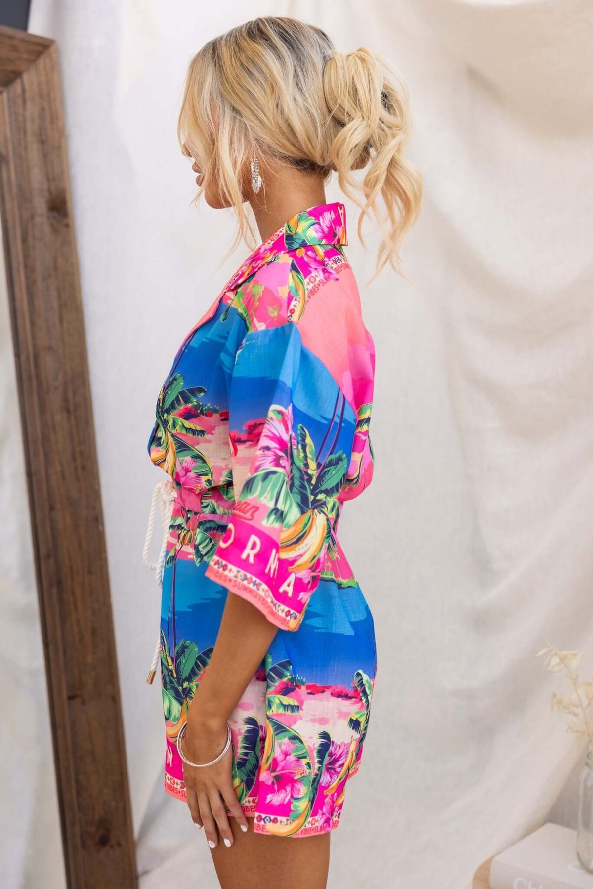 Side view of a vibrant holiday mode playsuit featuring a tropical print, button-down front, and relaxed fit.