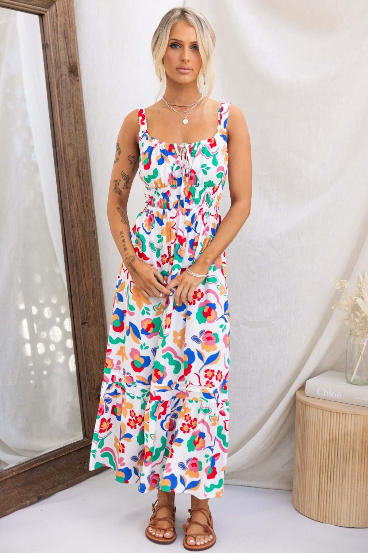 Model wearing Skipper Midi Dress with colorful floral print; adjustable straps, elastic waist, and light fabric.
