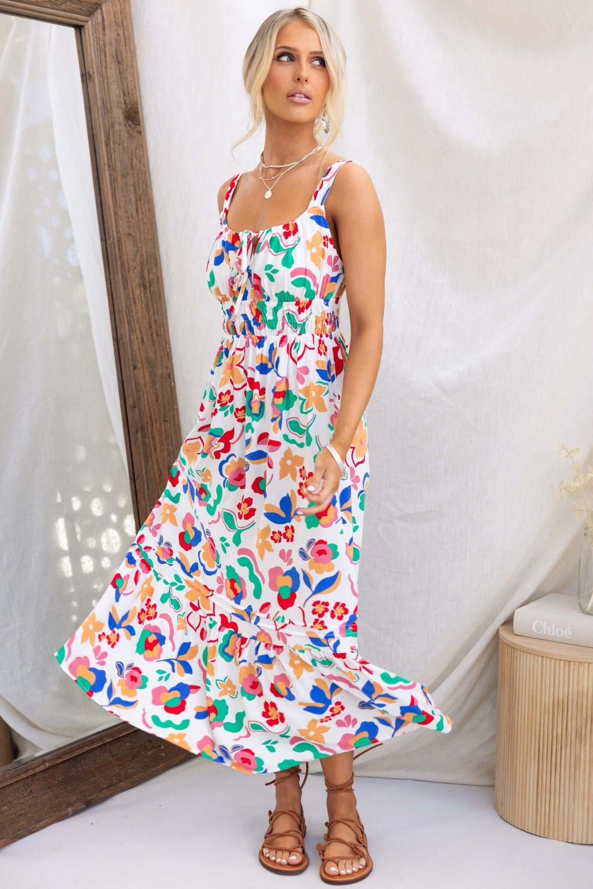 Model wearing Skipper Midi Dress with colorful floral print, adjustable straps, and tie detail at bust.