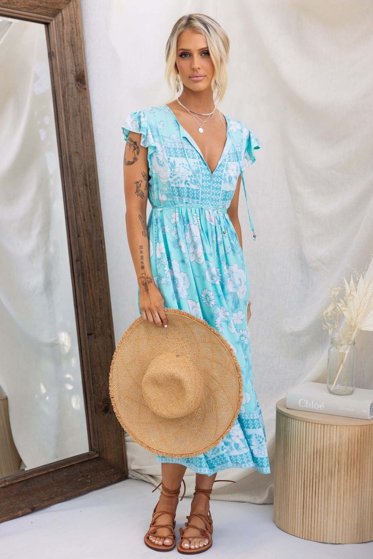 Model wearing a Coastal Breeze Maxi Dress in turquoise, holding a straw hat, styled with a natural background.