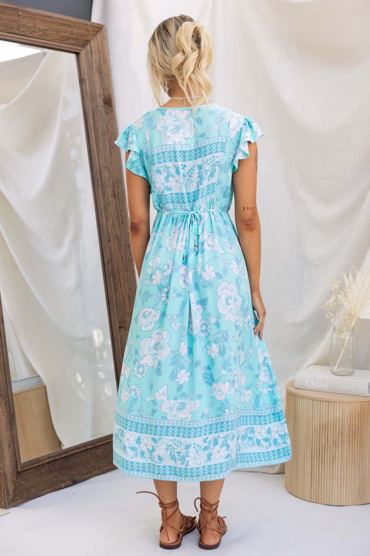 Back view of Coastal Breeze Maxi Dress in light blue floral print, featuring ruffled sleeves and a tied waist.