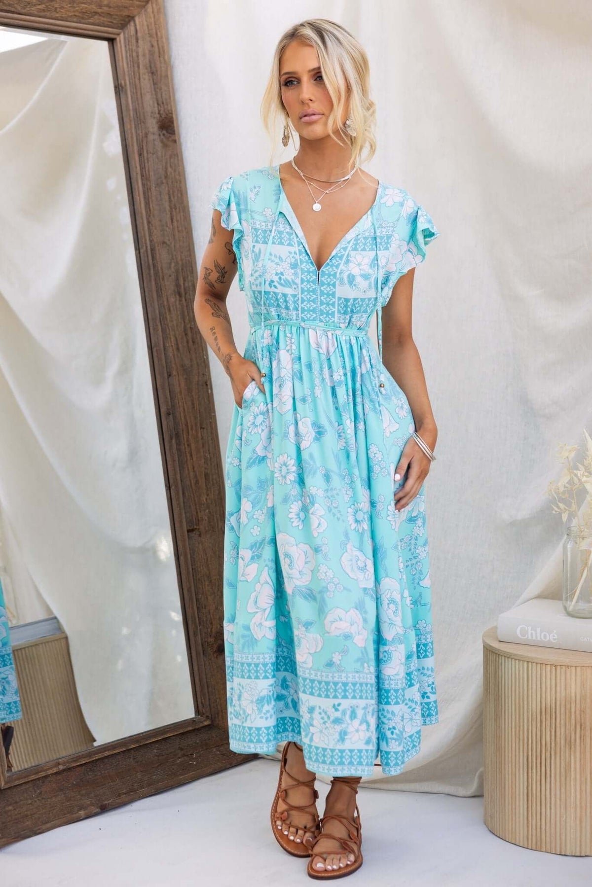 Model wearing a Coastal Breeze Maxi Dress with floral print and pockets, styled with sandals, in a bright, airy setting.