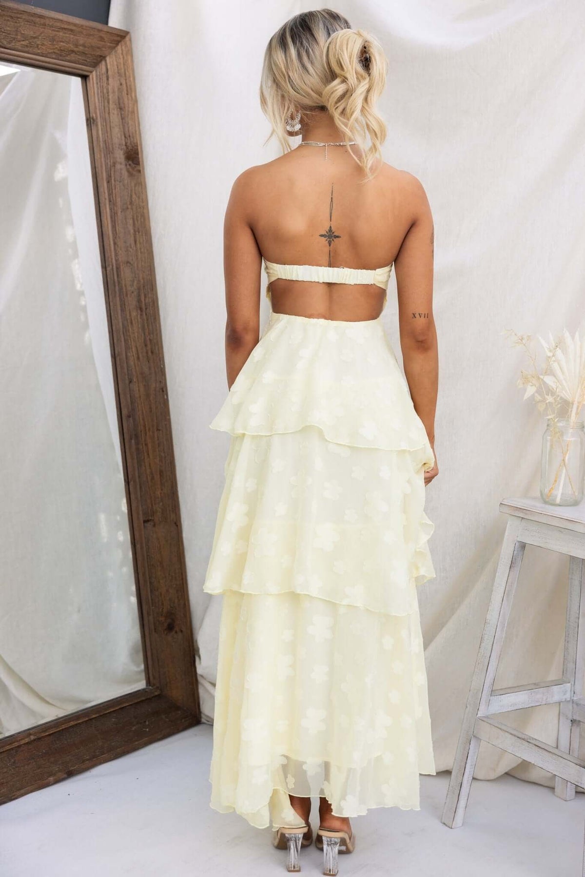 Back view of a model wearing a soft yellow Soft Whispers Maxi Dress with tiered ruffles and a cut-out design.