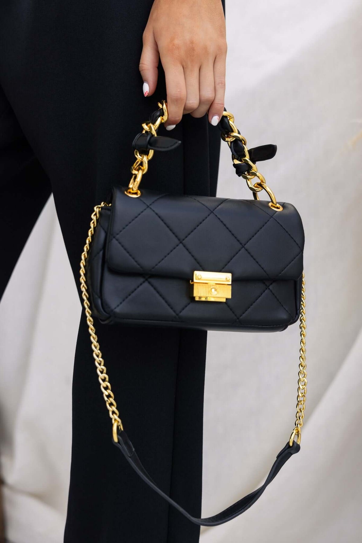 Stylish black Ari Bag featuring a chunky handle with gold chain accents and quilted vegan leather design.