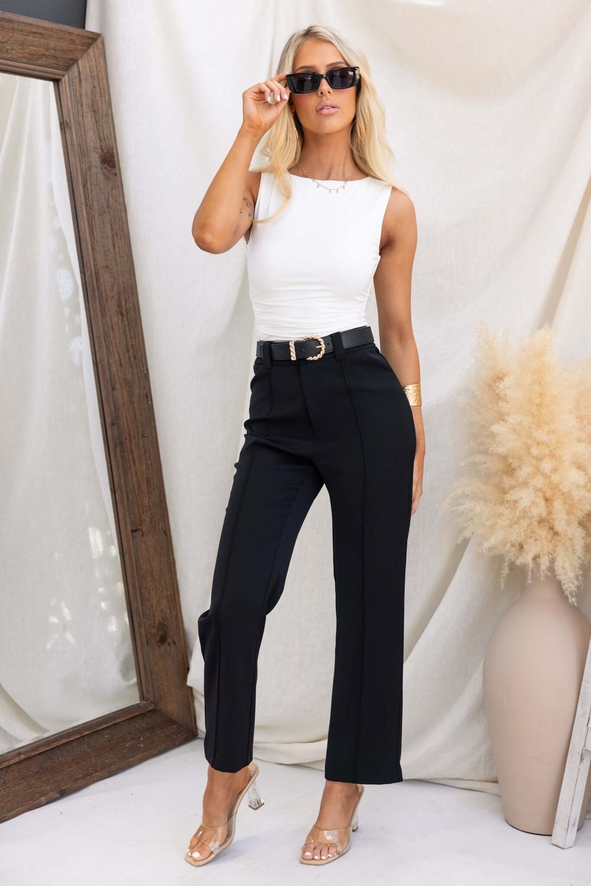 Woman styled in Columbus Pants, black mid-high waist trousers, paired with a white top and sunglasses, set against a neutral background.