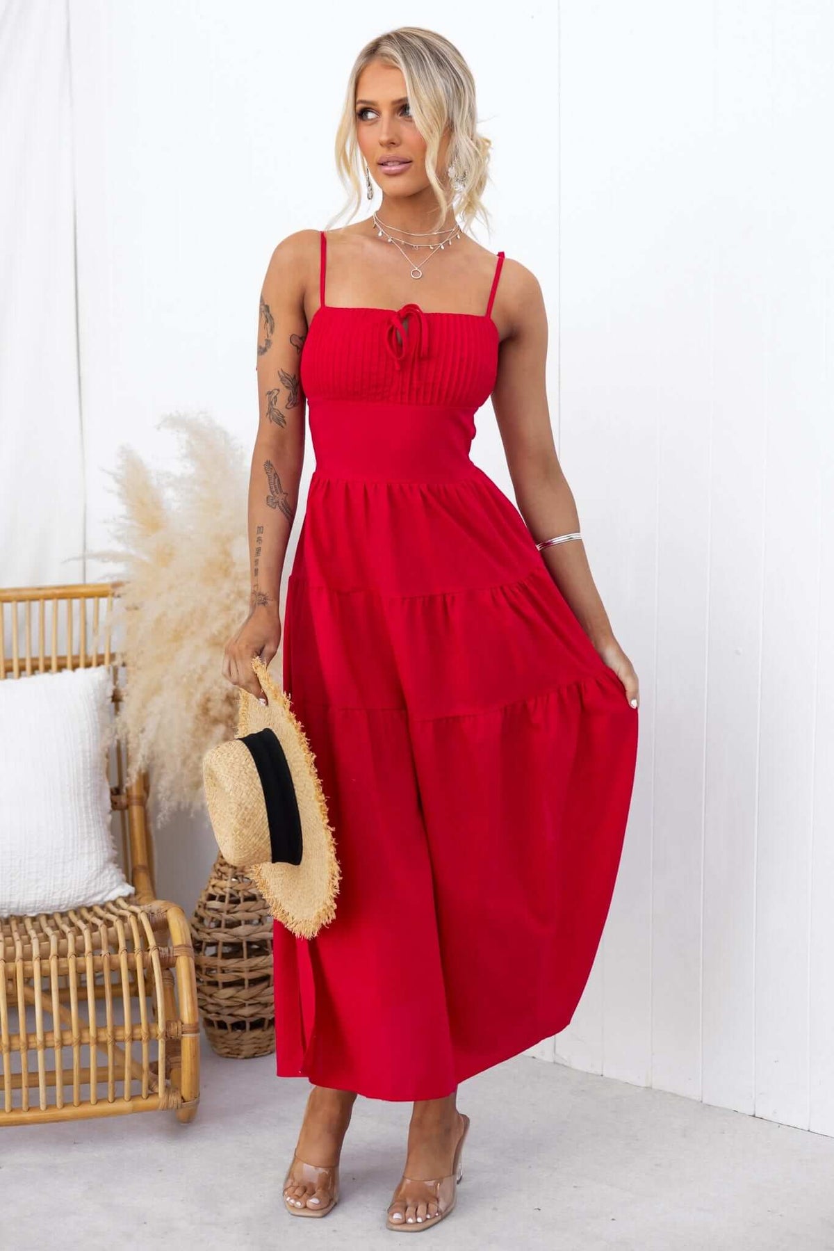 Model wearing Gresham Maxi Dress in red with thin tie straps and side splits, accessorized with a straw hat.