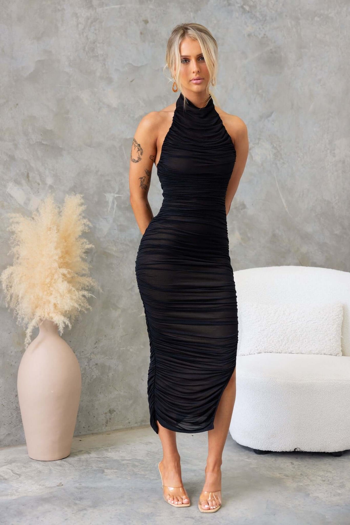 Black Gellis Midi Dress with high neckline, buttons, and asymmetric hemline, styled in a chic setting.