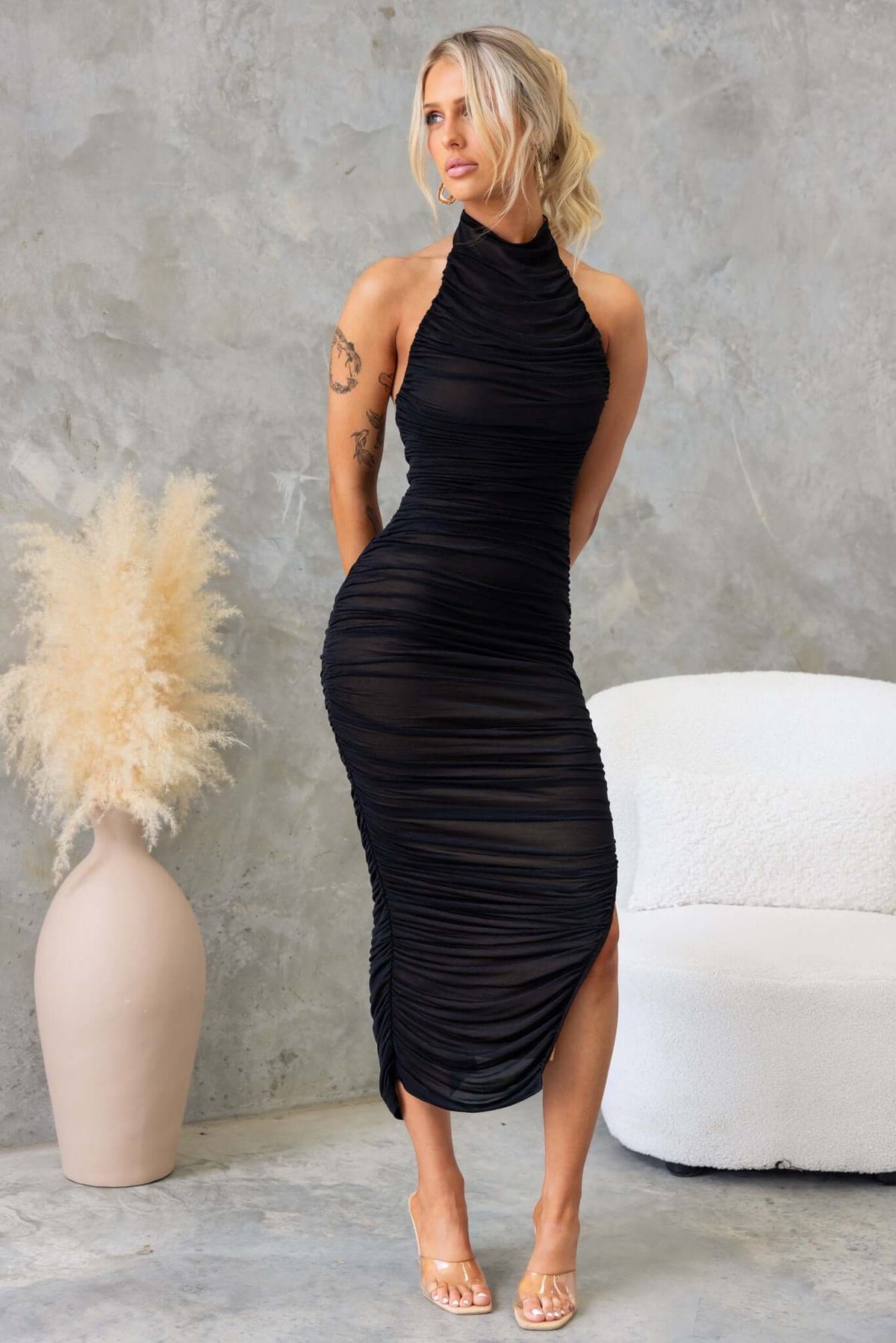 Gellis Midi Dress in black, featuring high neckline, side zip, and asymmetric hemline, displayed by a model.