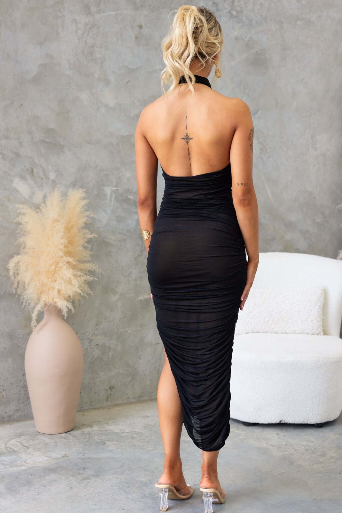 Model showcasing the back view of a black Gellis Midi Dress with high neckline and asymmetrical hemline.