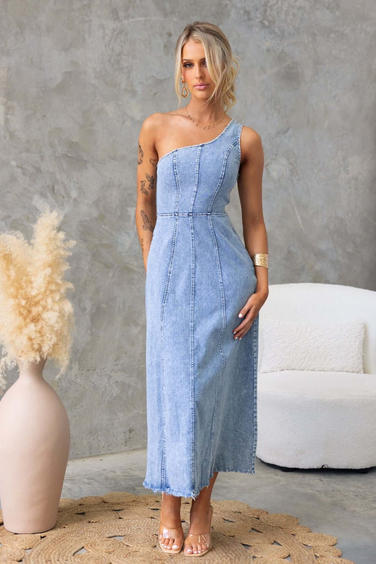 One-shoulder denim maxi dress with raw hemline, styled elegantly with removable brooch.
