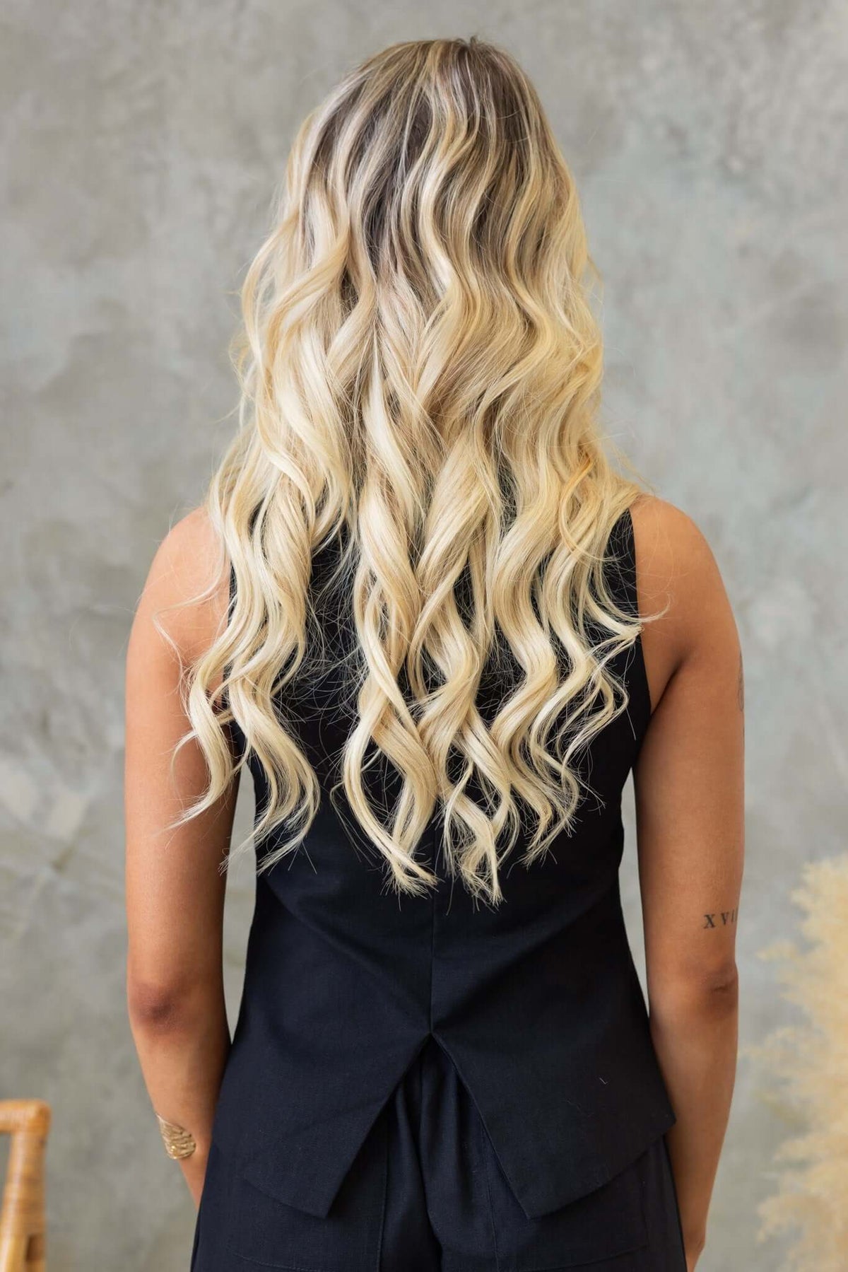 Woman with long wavy blonde hair wearing a black button down top from the back, showcasing a stylish and casual look.