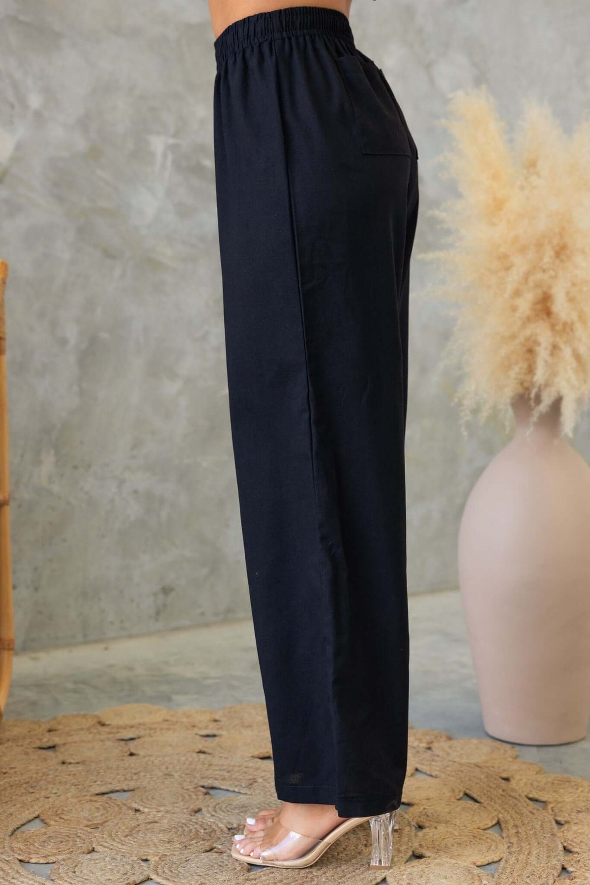Side view of black Payson Pants featuring an elastic waist, drawstring tie, and back pockets against a textured background.