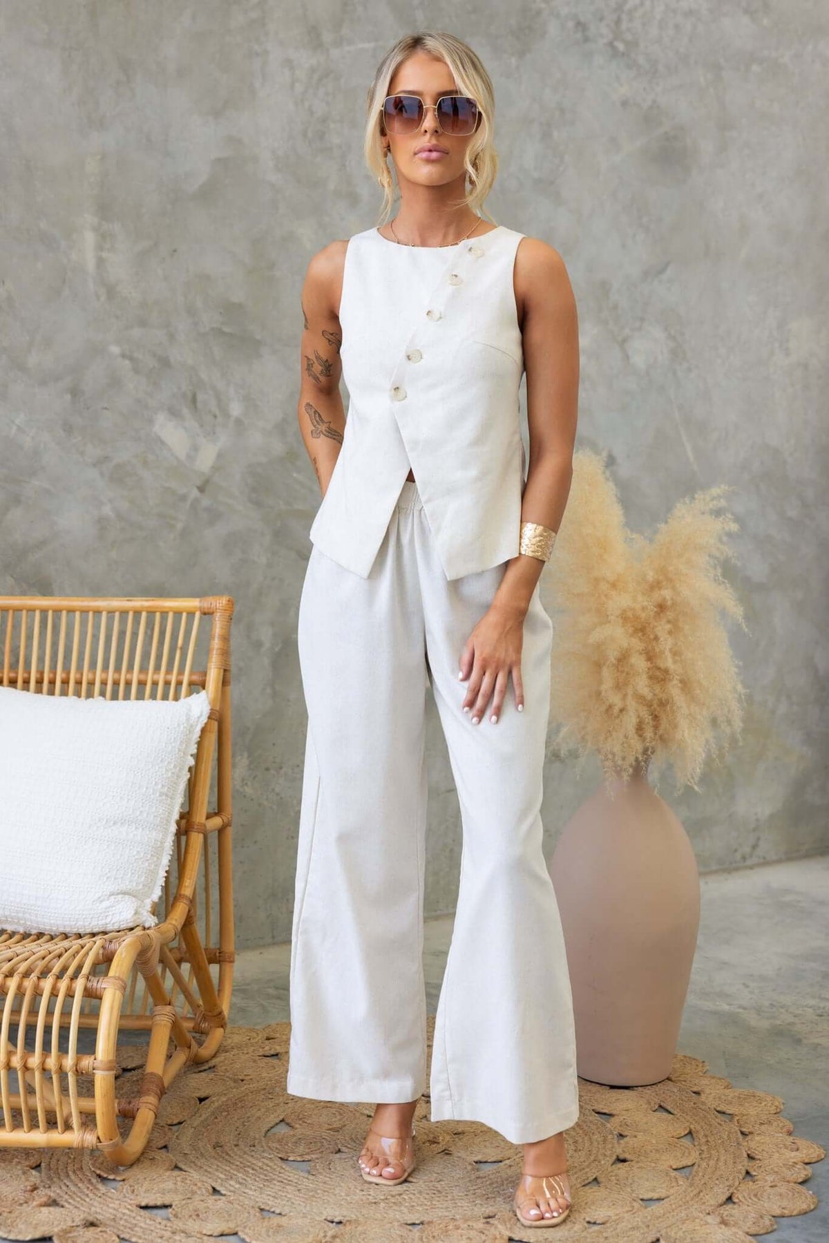 Model wearing a button-down Payson Top with a linen look, paired with white wide-leg pants, styled with sunglasses.