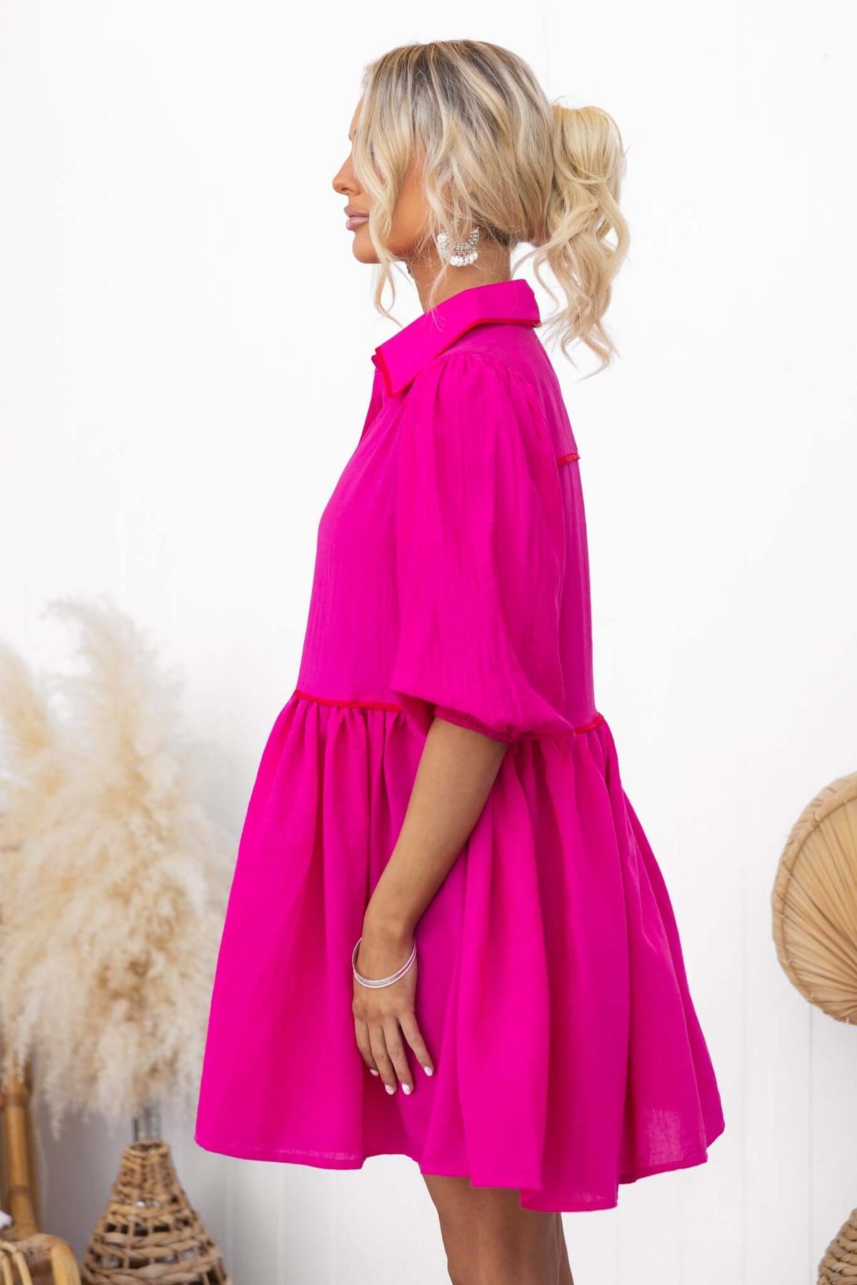 Profile view of a woman wearing a bright pink Sherbet Dress with a button-down front and puff sleeves.