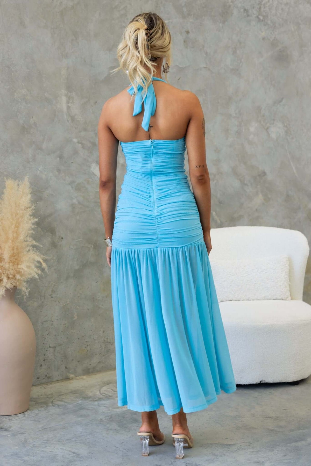 Back view of the Fate Maxi Dress in light blue, featuring a tie neck and ruched bodice with a flowing skirt.