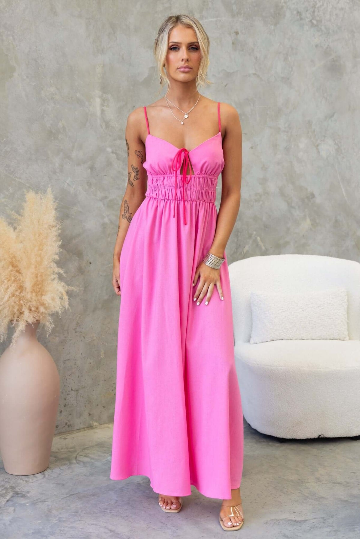 Model wearing a pink Brooklynn Maxi Dress with adjustable straps and tie front detail against a neutral backdrop.