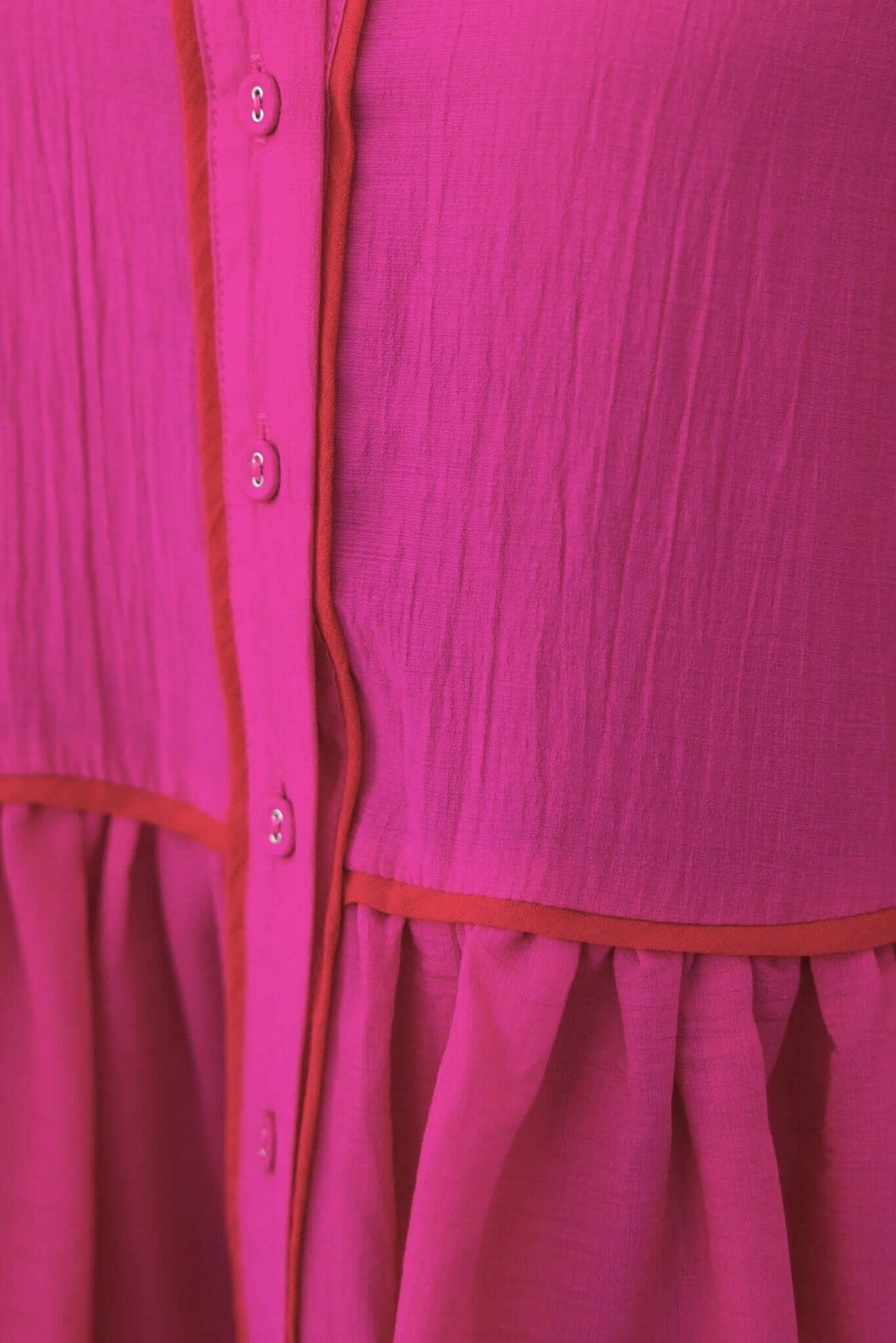 Close-up of a vibrant pink Sherbet Dress with button details and contrasting trim, showcasing its lightweight, flowing material.