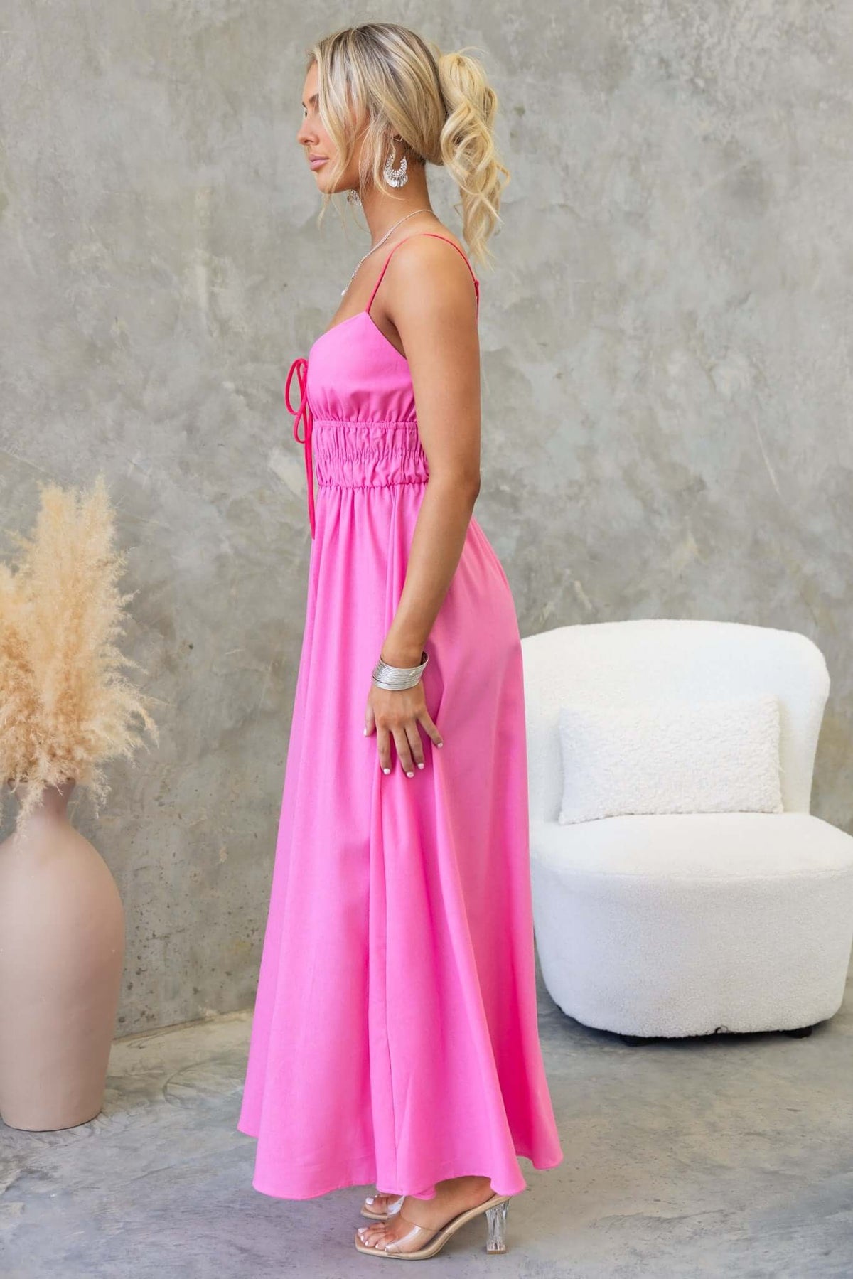 Brooklynn Maxi Dress in vibrant pink, featuring adjustable straps, tie detail, and elastic waist, styled against a neutral backdrop.