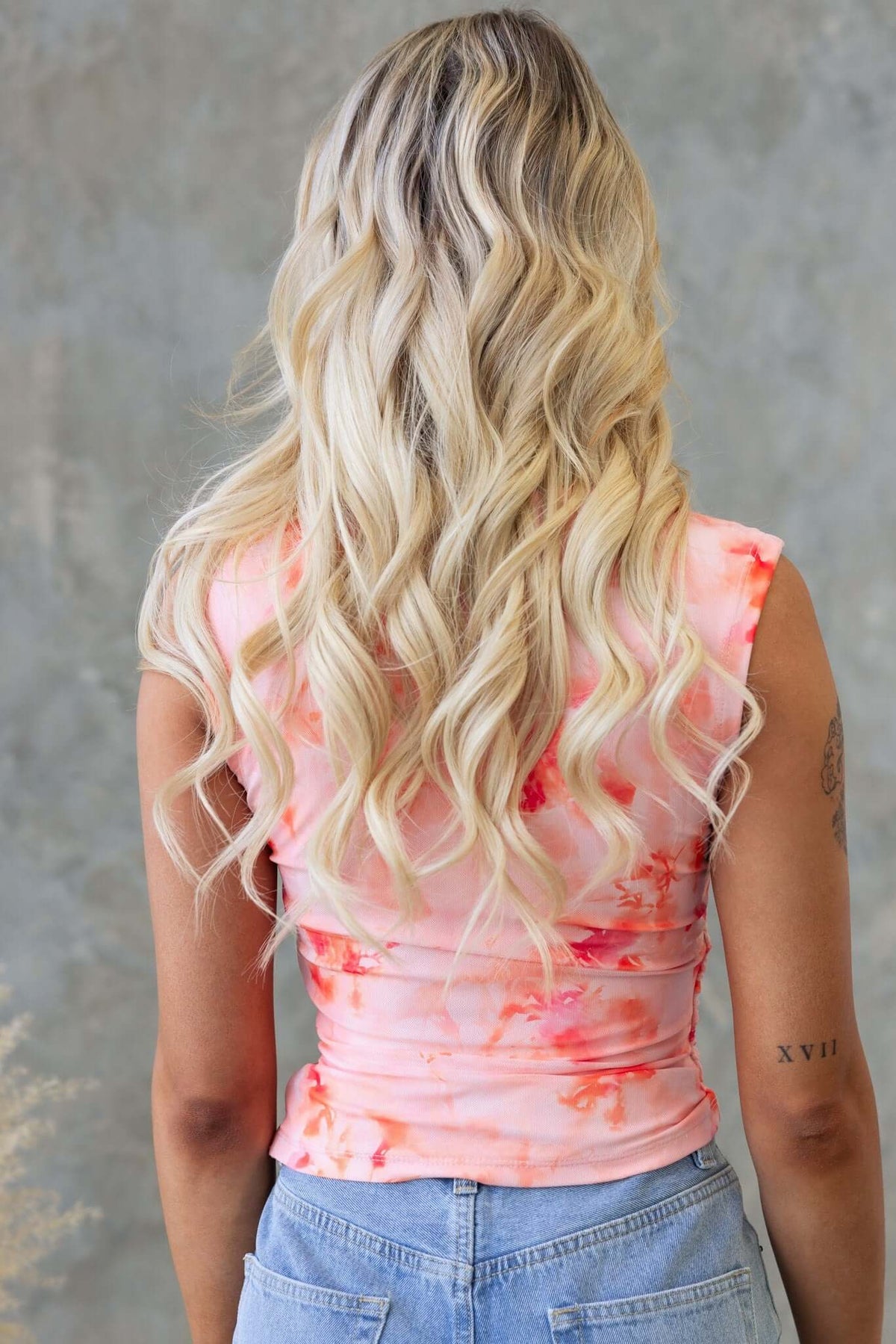 Back view of a woman wearing a pink floral Cosmo Top with a round neckline and wavy hair.