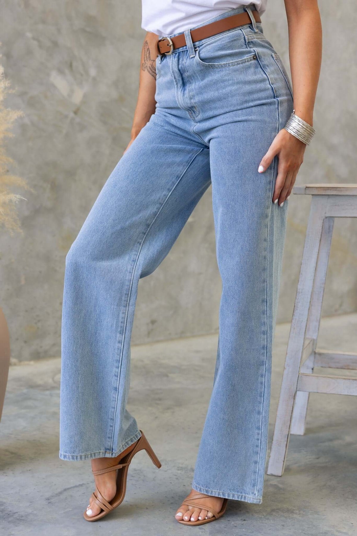 Claremont Jeans featuring a high waist, wide straight leg, zip button closure, styled with a brown belt and sandals.