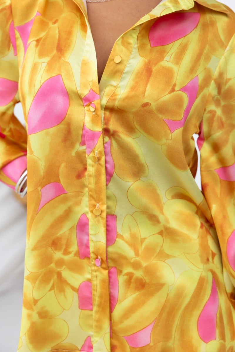 Indianna Top features a vibrant satin shirt with floral yellow and pink print, button-up front, and side splits.
