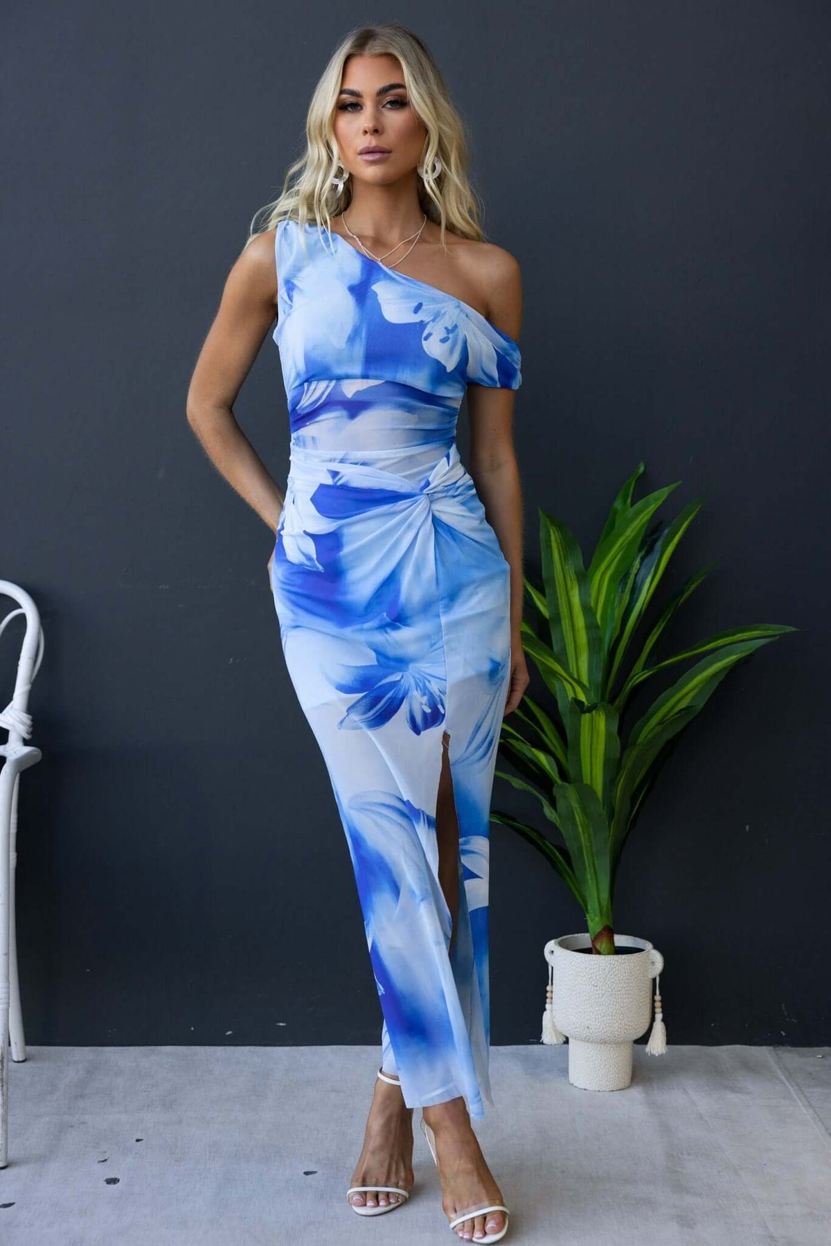 Model wearing the Escala Maxi Dress with asymmetric neckline and floral print, featuring a front split and knot detail.
