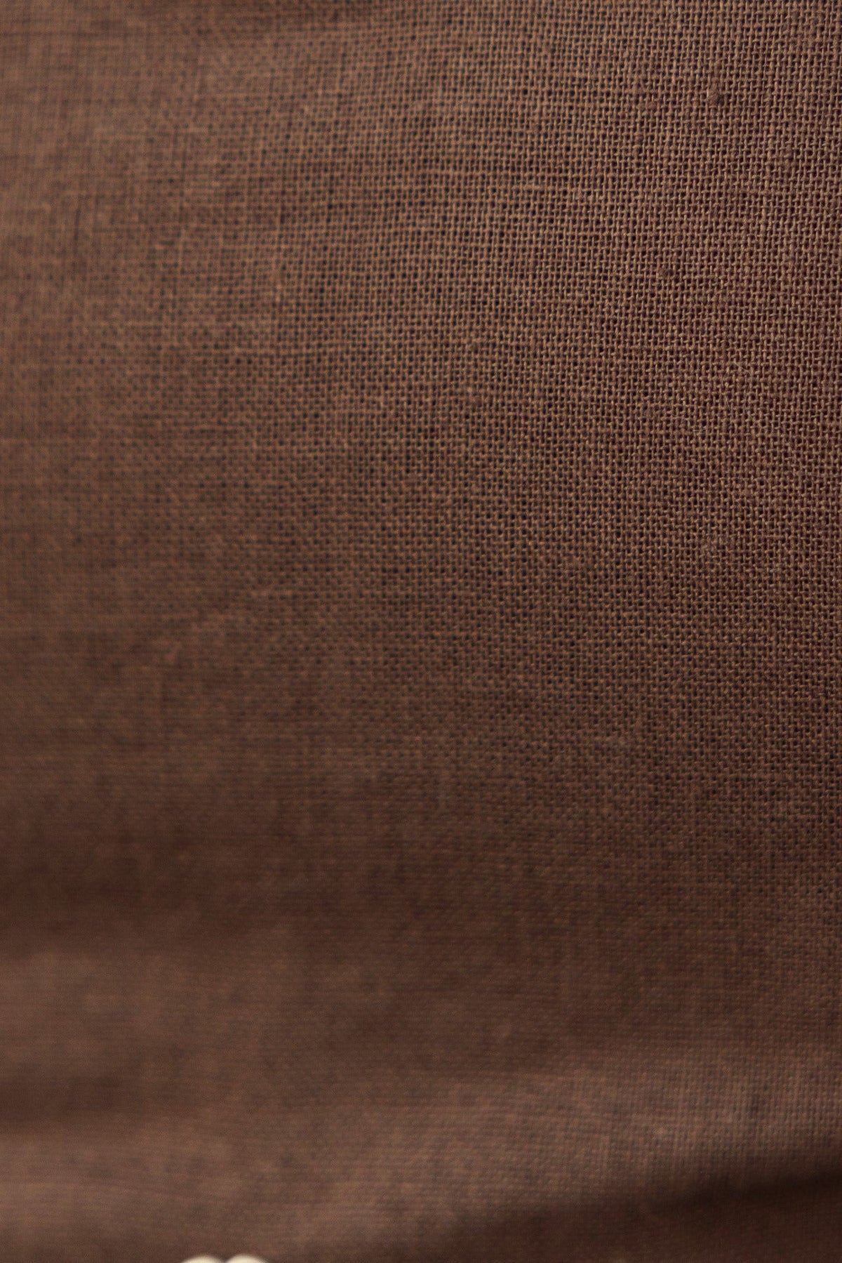 Close-up of textured brown linen fabric, showcasing a rich weave and soft finish, ideal for stylish clothing.