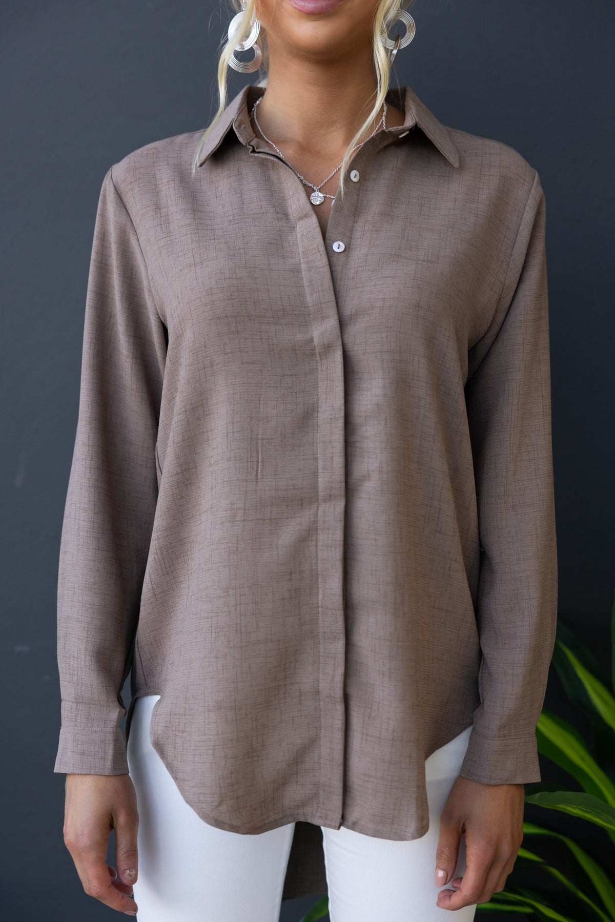 A model wearing a brown button-up Toomba shirt, featuring a collar and a slightly relaxed fit, paired with white pants.