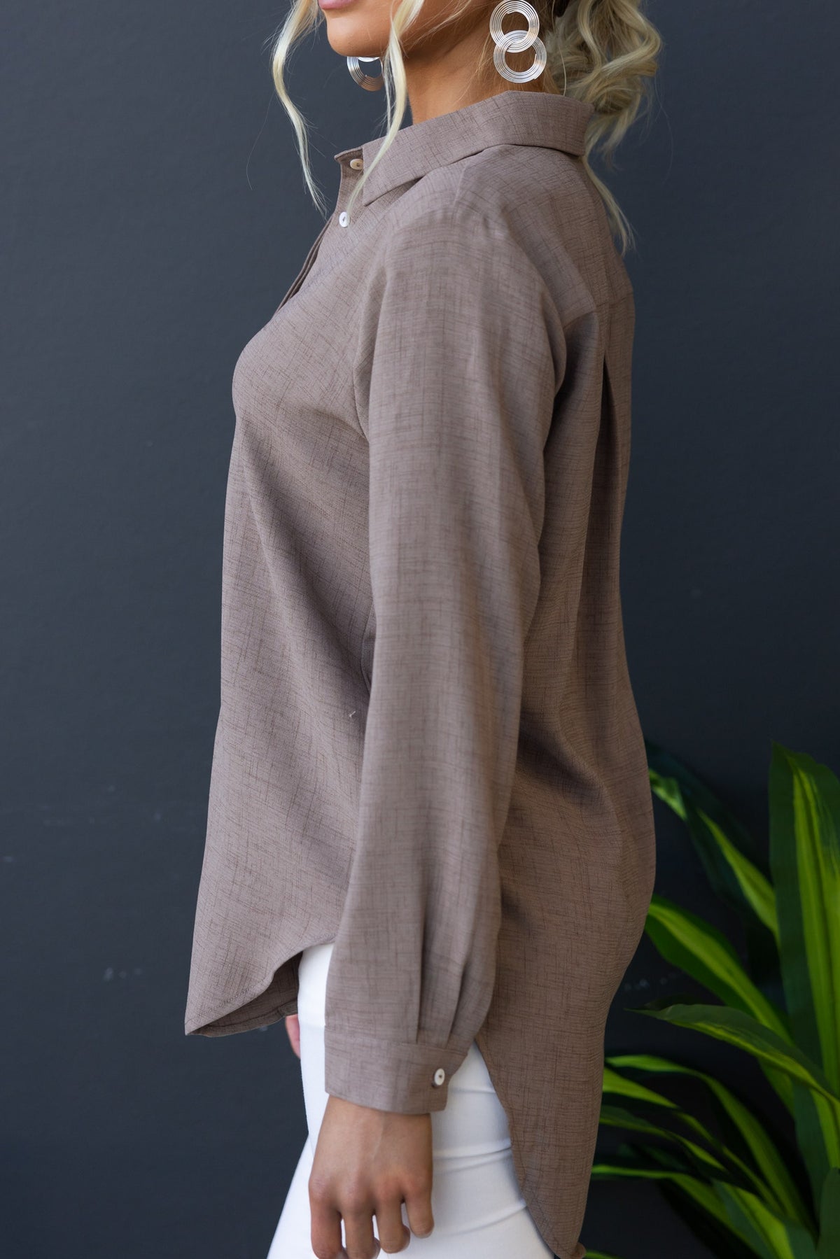 Side view of Toomba Shirt, a light brown button-up shirt made of soft polyester, styled with white pants and earrings.