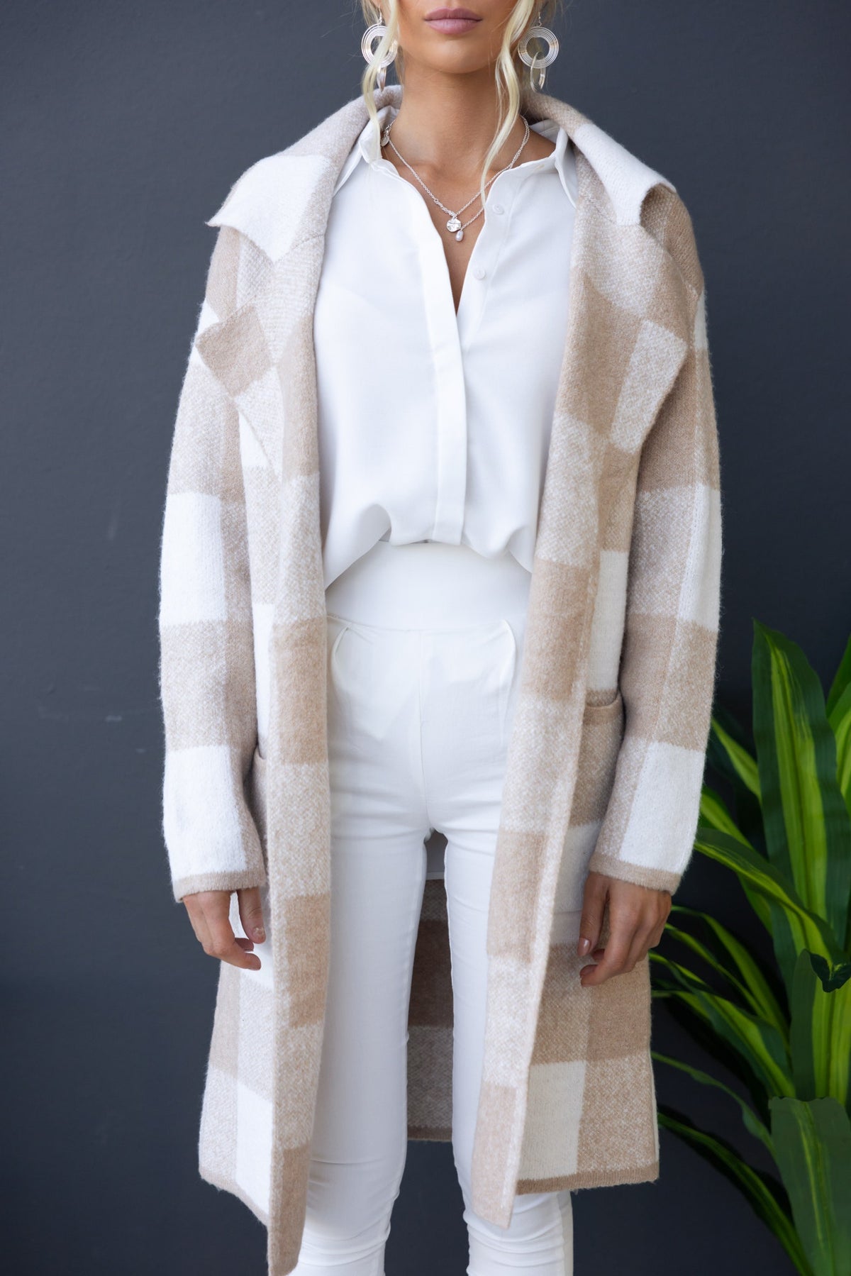 Fatale Cardigan in beige and white plaid, featuring a longline fit, collar, and pockets, styled with white pants and a shirt.