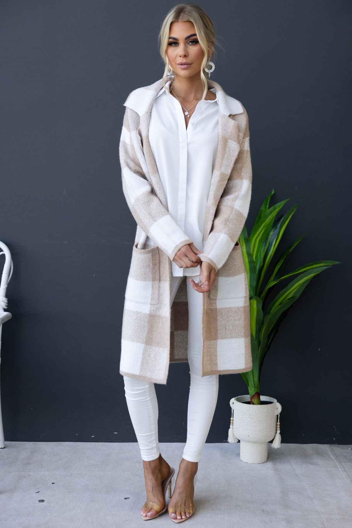 Model wearing a longline Fatale Cardigan in beige and white check, styled with a white shirt and white pants.