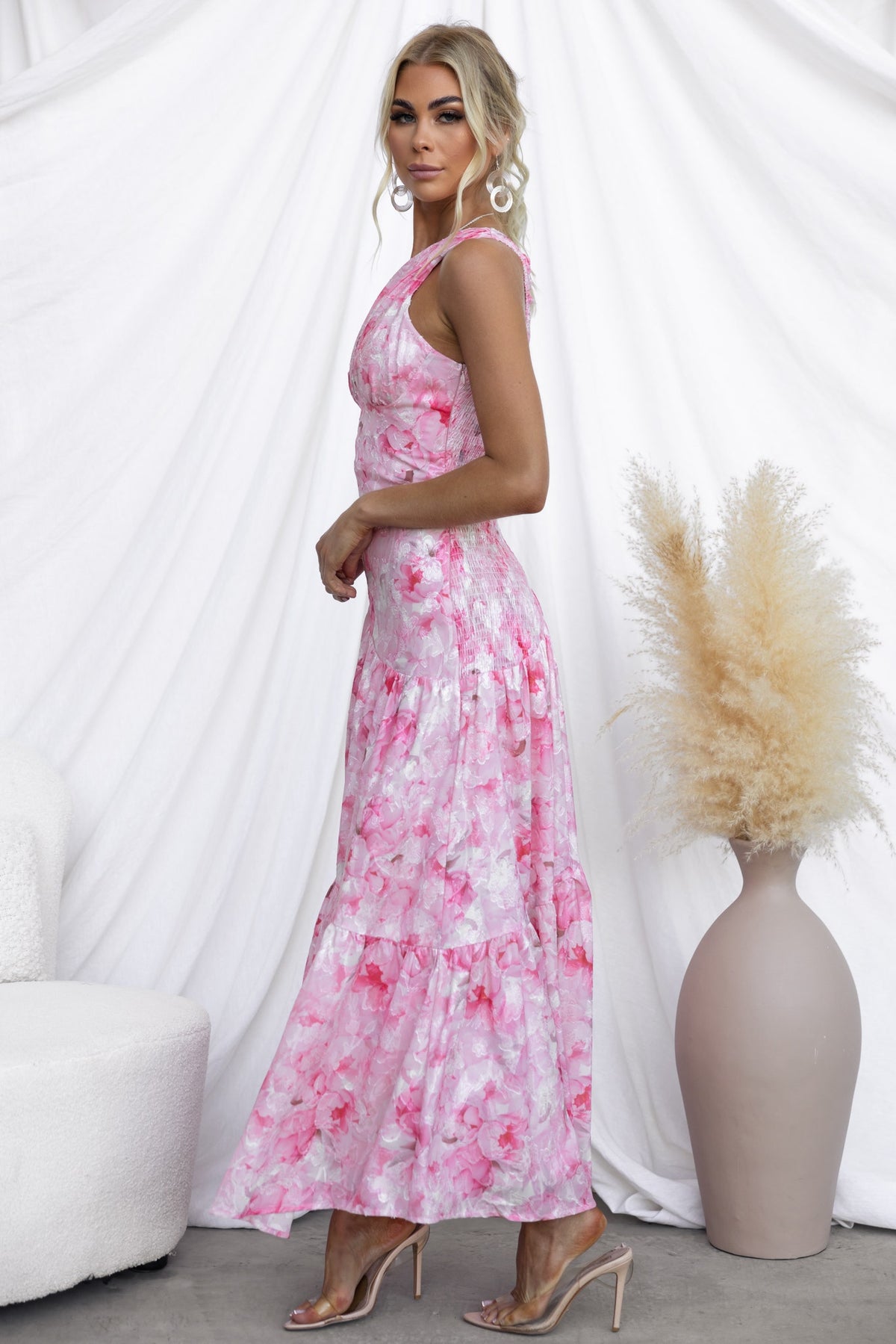 Model wearing the Asja Maxi Dress, featuring a one-shoulder design and pink floral pattern, styled in a modern setting.