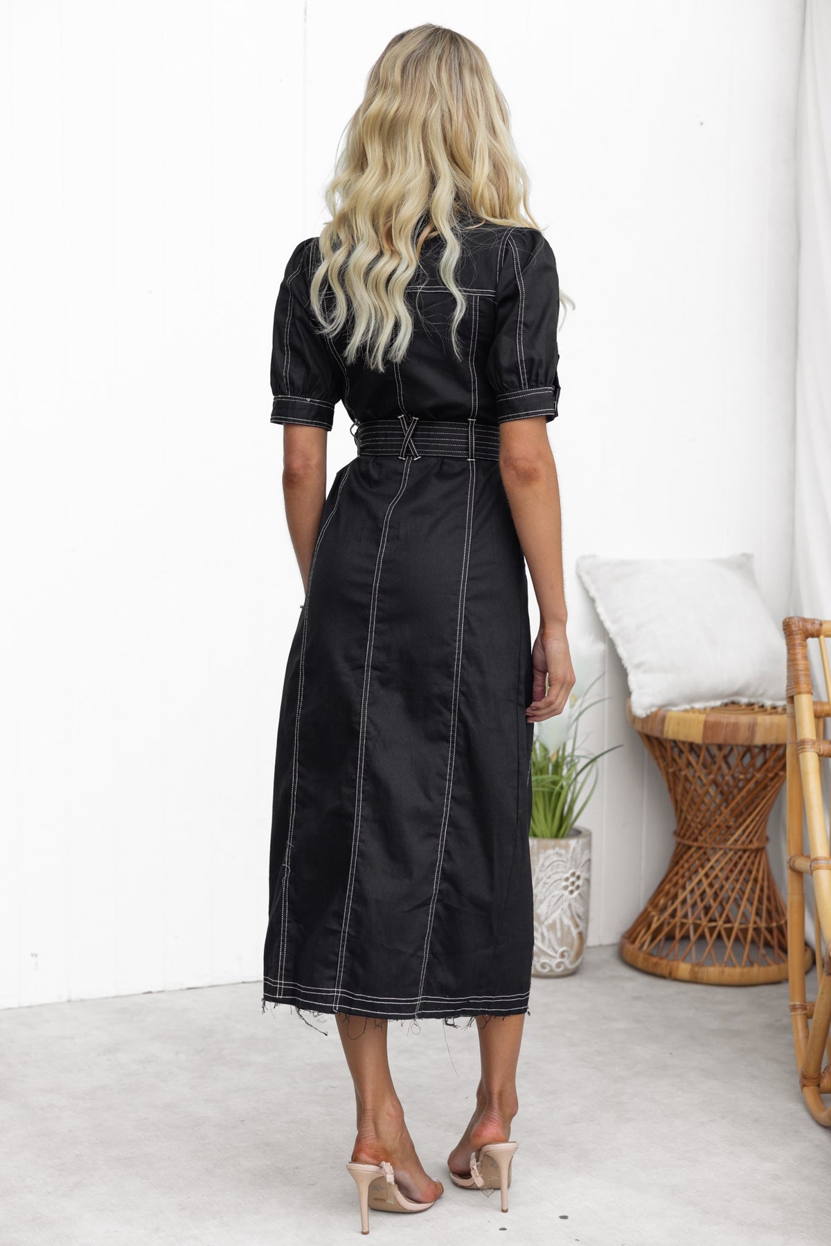 Back view of a black denim midi dress featuring a frayed hem, button-up front, and a removable belt.