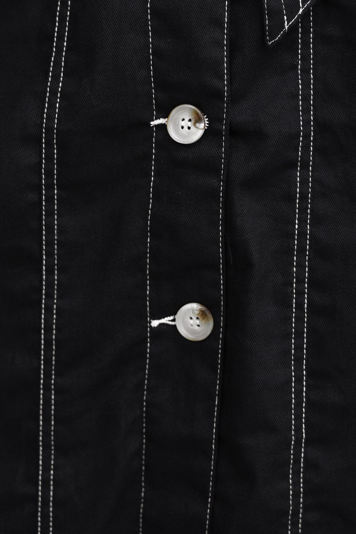 Close-up of black denim fabric featuring two silver buttons and contrasting white stitching.