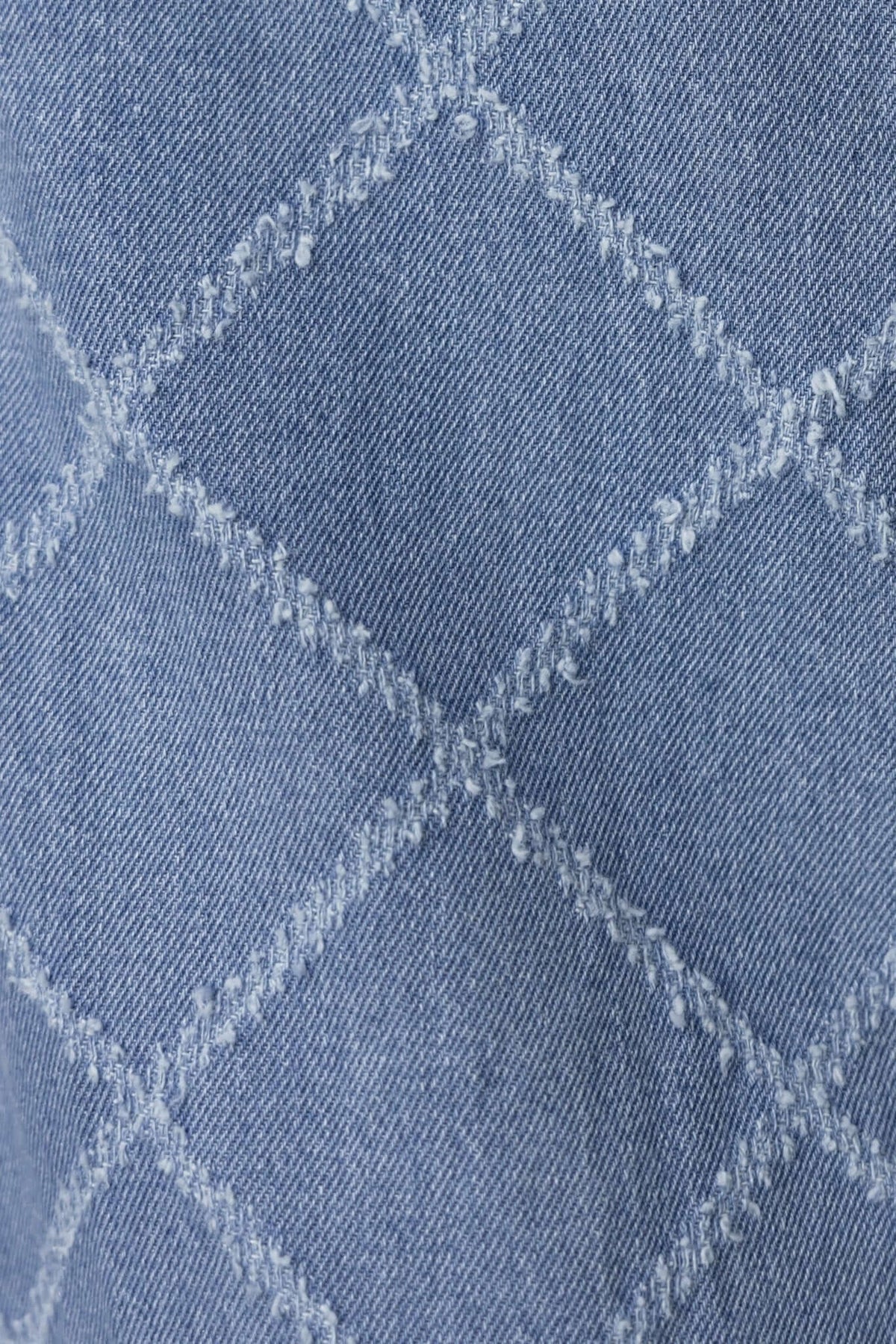 Close-up of denim fabric featuring a diamond quilted pattern, showcasing texture and stitching detail.