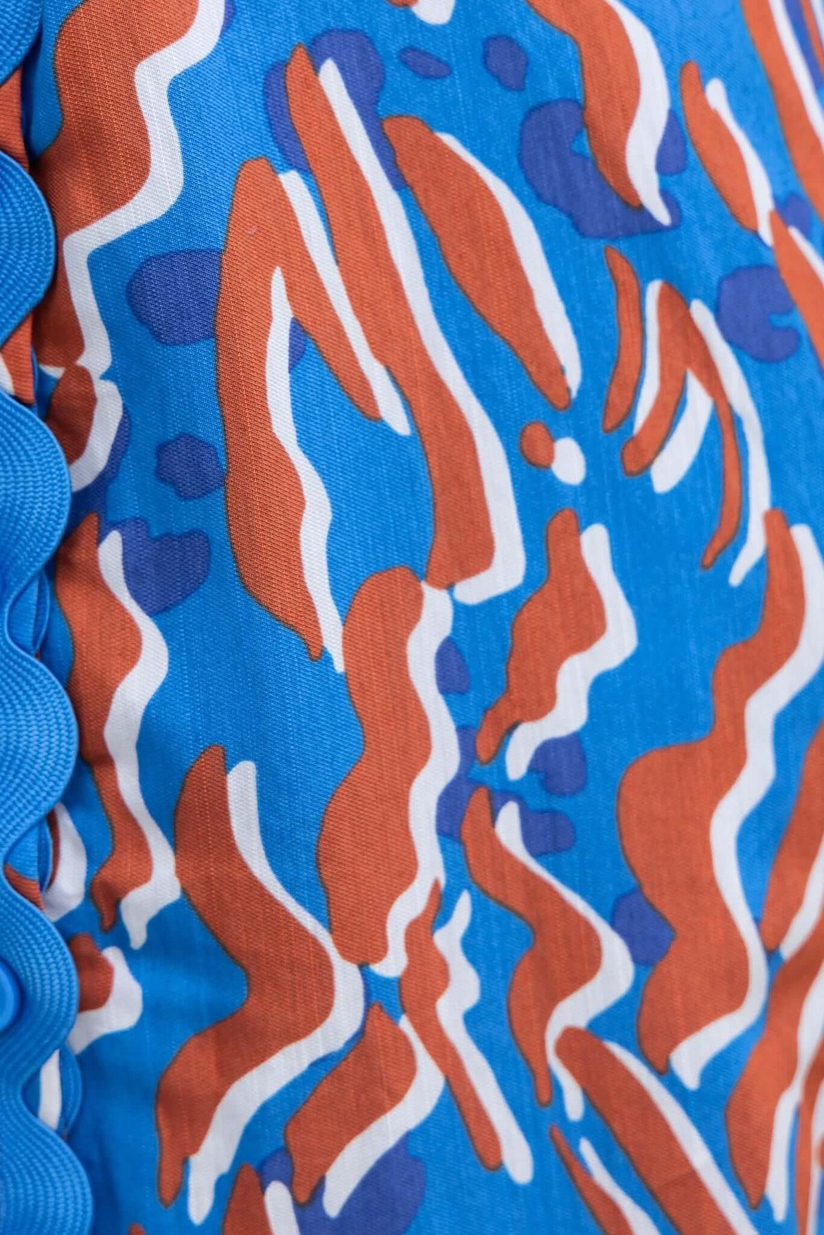 Colorful blue and brown abstract pattern fabric with scalloped edge detail, ideal for making stylish dresses.