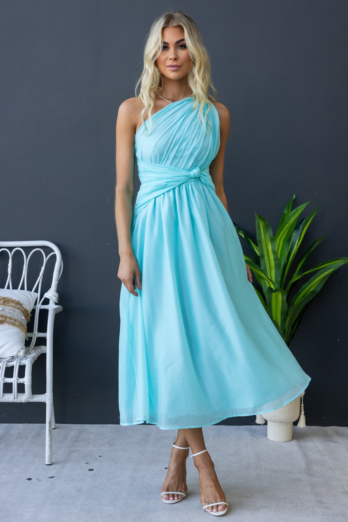 Model wearing a light blue Arturo Midi Dress with one-shoulder neckline and front knot, styled with heels.