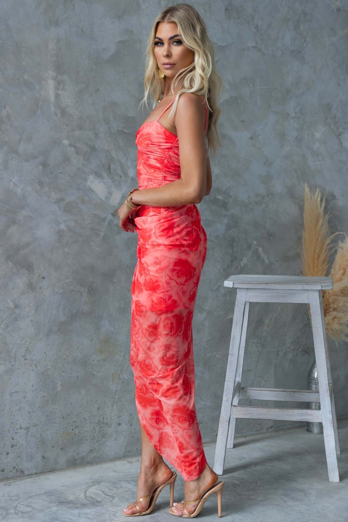 Model wearing the Saloni Maxi Dress in vibrant red with floral patterns, featuring adjustable straps and an asymmetric hemline.