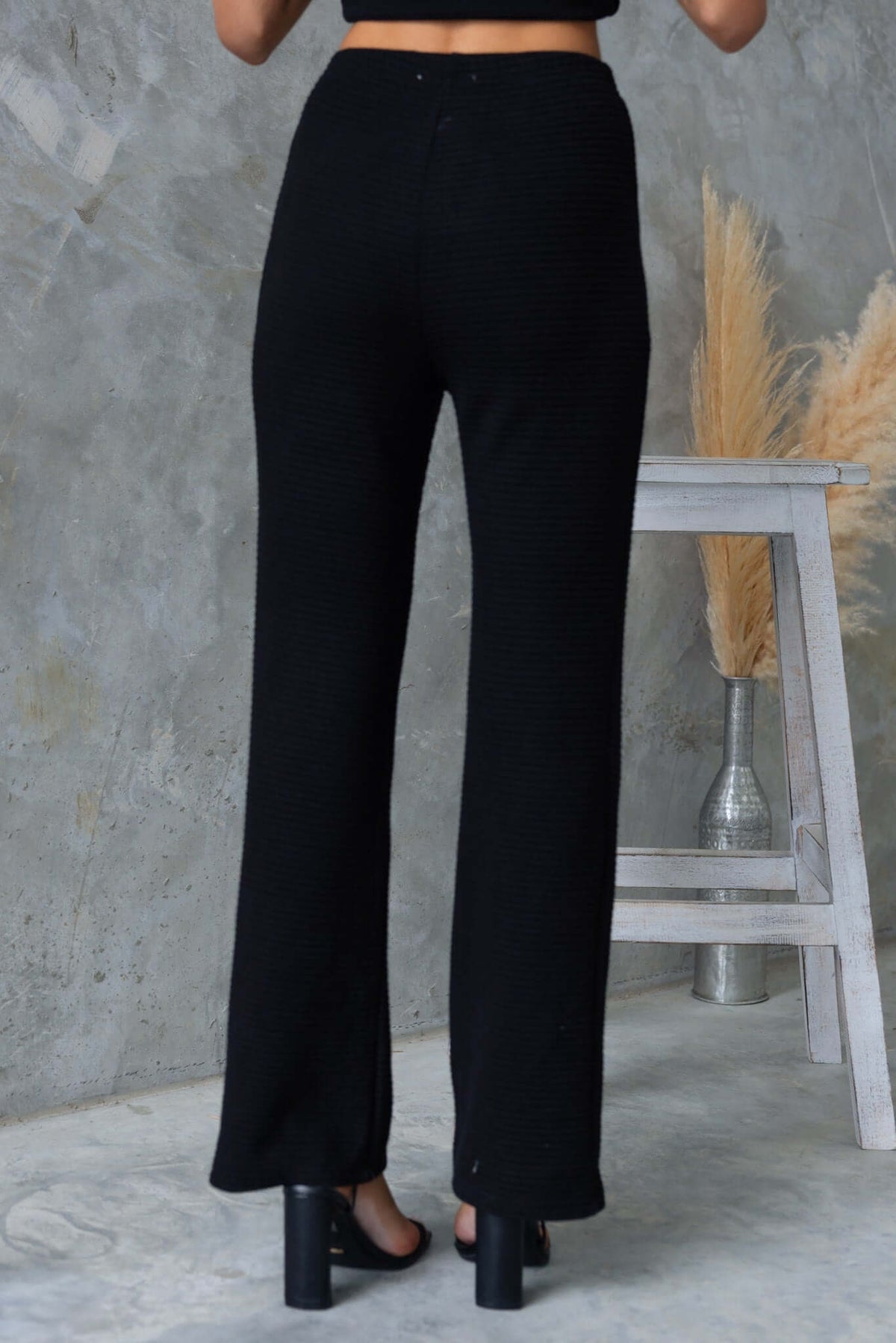 Back view of Xandra Pants, black mid-high waist pants with drop-crotch style, elastic waistband, and stretch knit material.