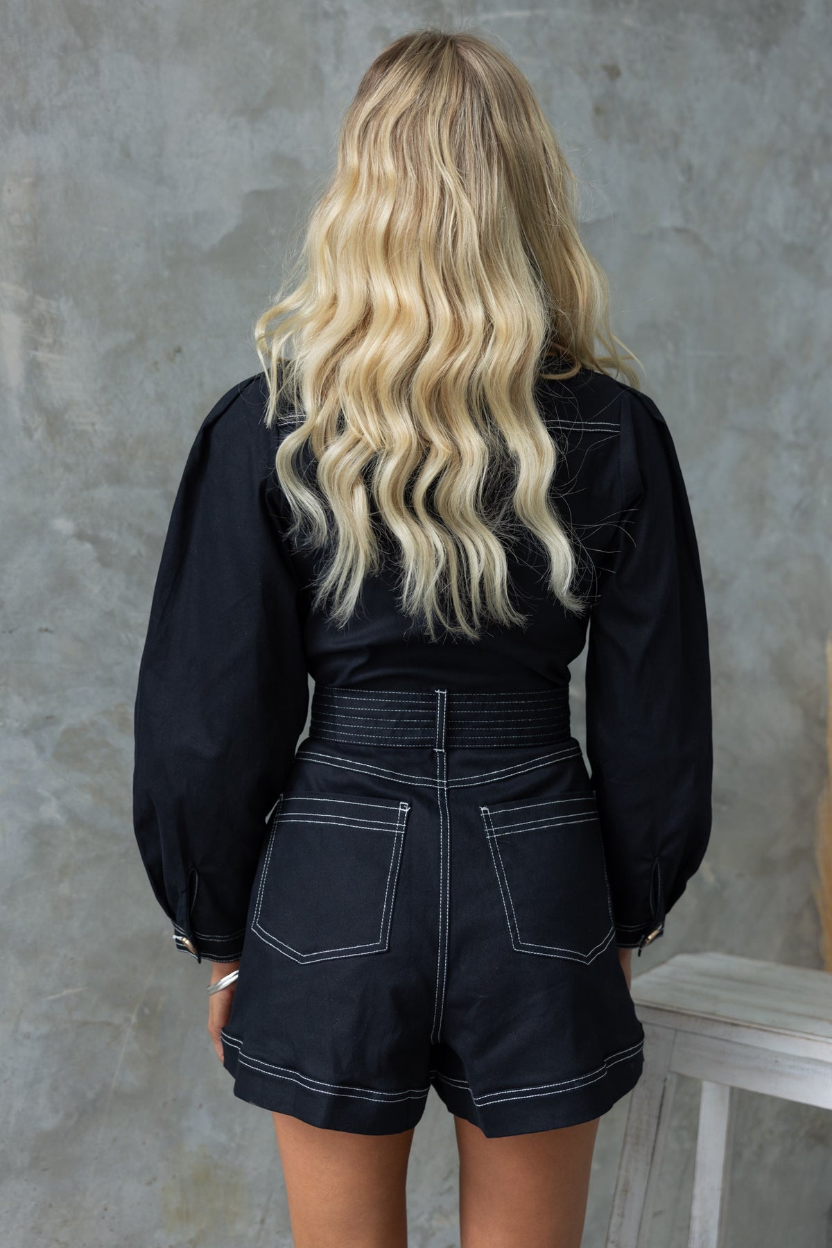 Model wearing black denim Pina playsuit with puff sleeves and elastic waistband, showcasing a stylish back view.