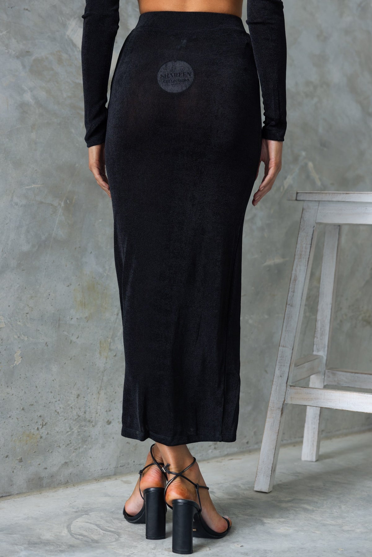 Back view of Burnette black maxi skirt featuring a mid-high waist and split design, styled with strappy heels.