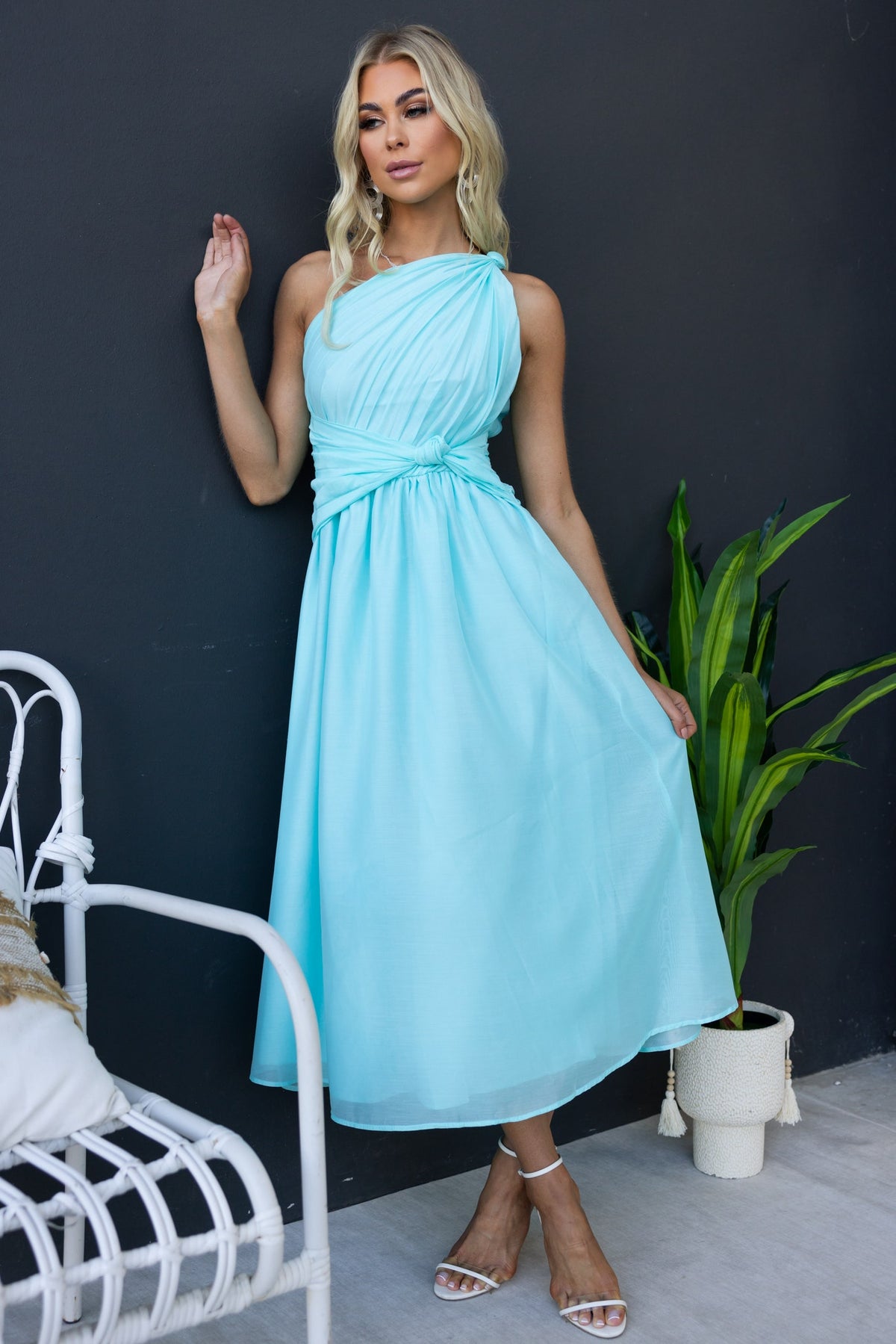Model in an aqua Arturo Midi Dress featuring a one-shoulder neckline and front knot, styled with a plant backdrop.