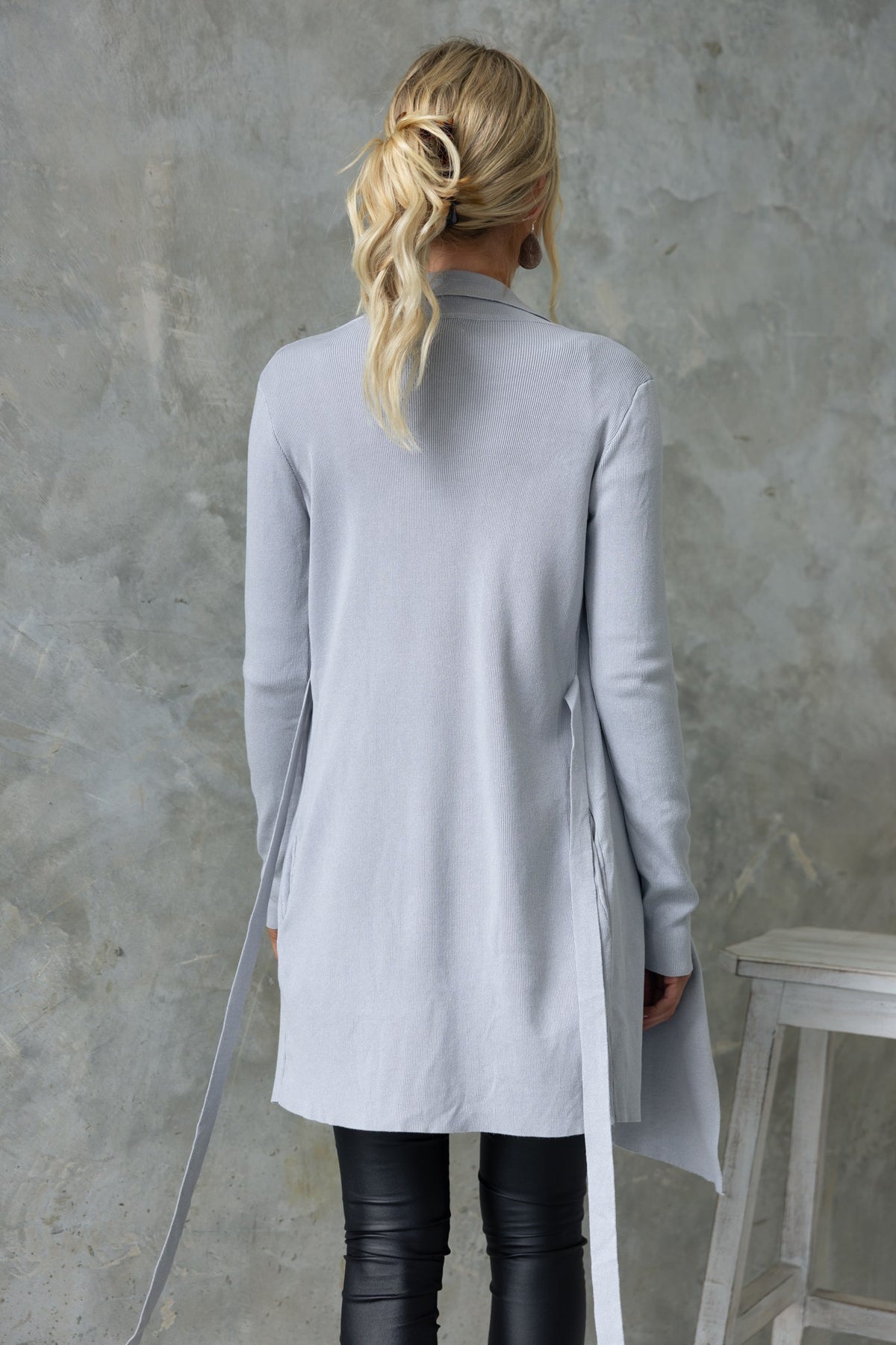 Back view of Acaia Cardigan in light grey with attached belt and slightly relaxed fit, styled with black leather pants.