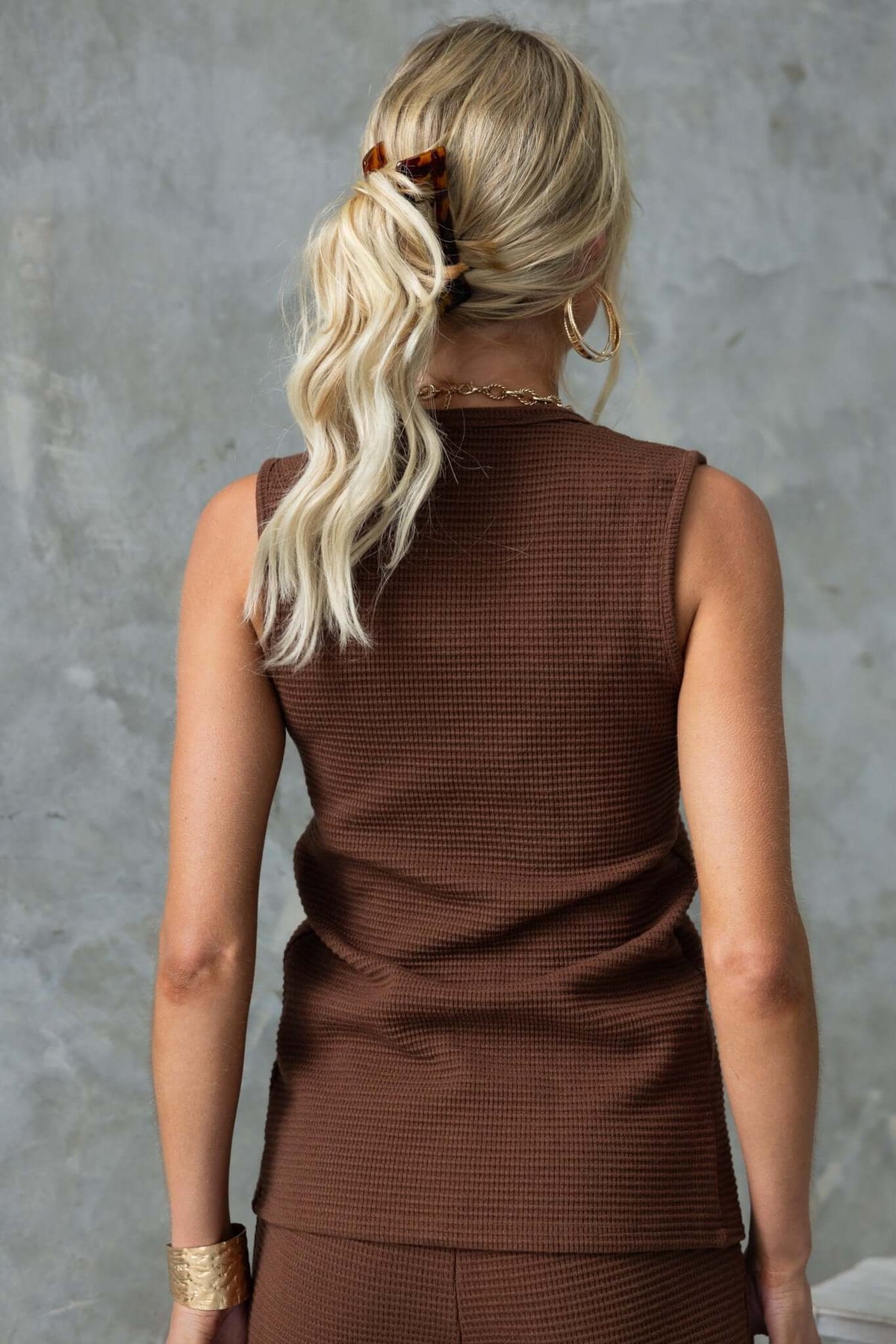 Back view of a woman wearing the Xandra Top, a brown knit vest with a fitted silhouette.