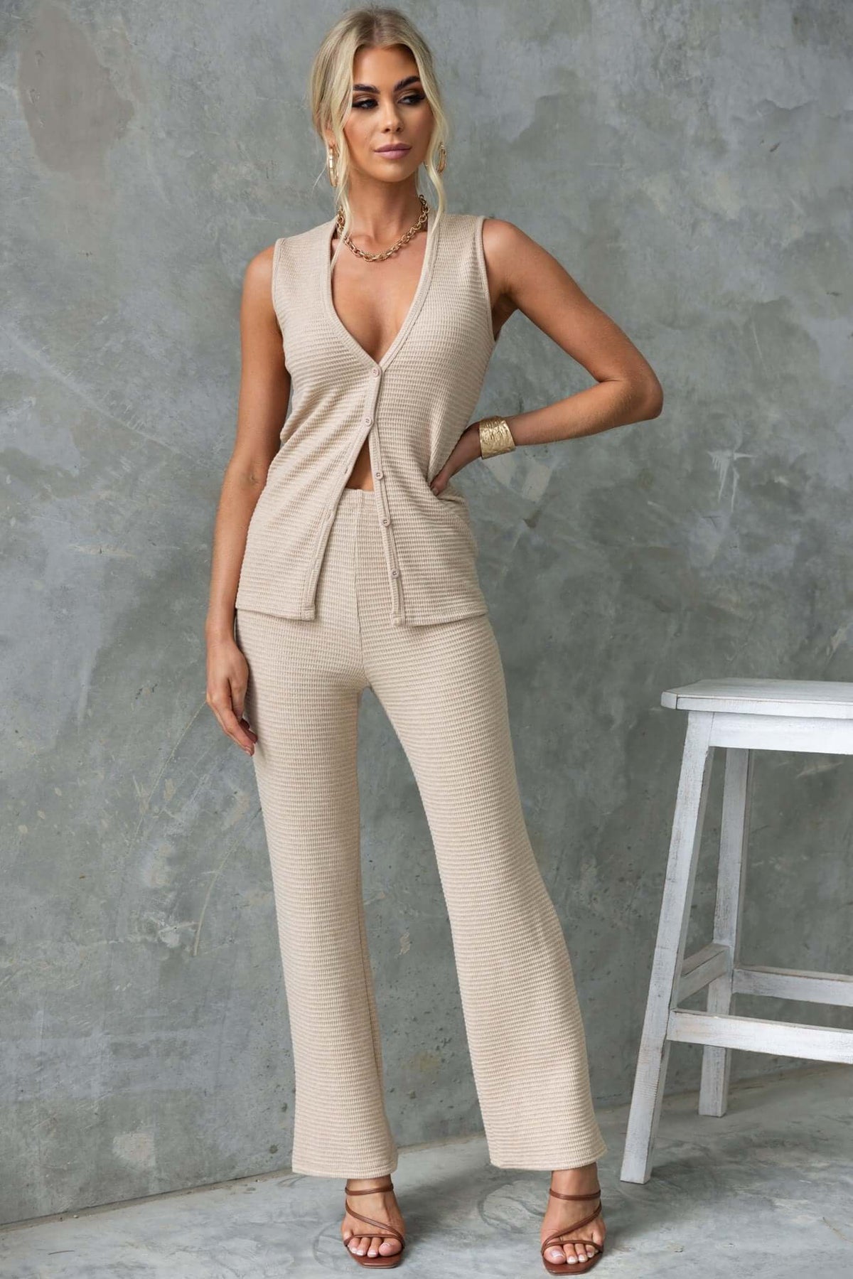 Stylish woman in beige Xandra Pants outfit, featuring a mid-high waist and drop-crotch style, posed against a textured background.
