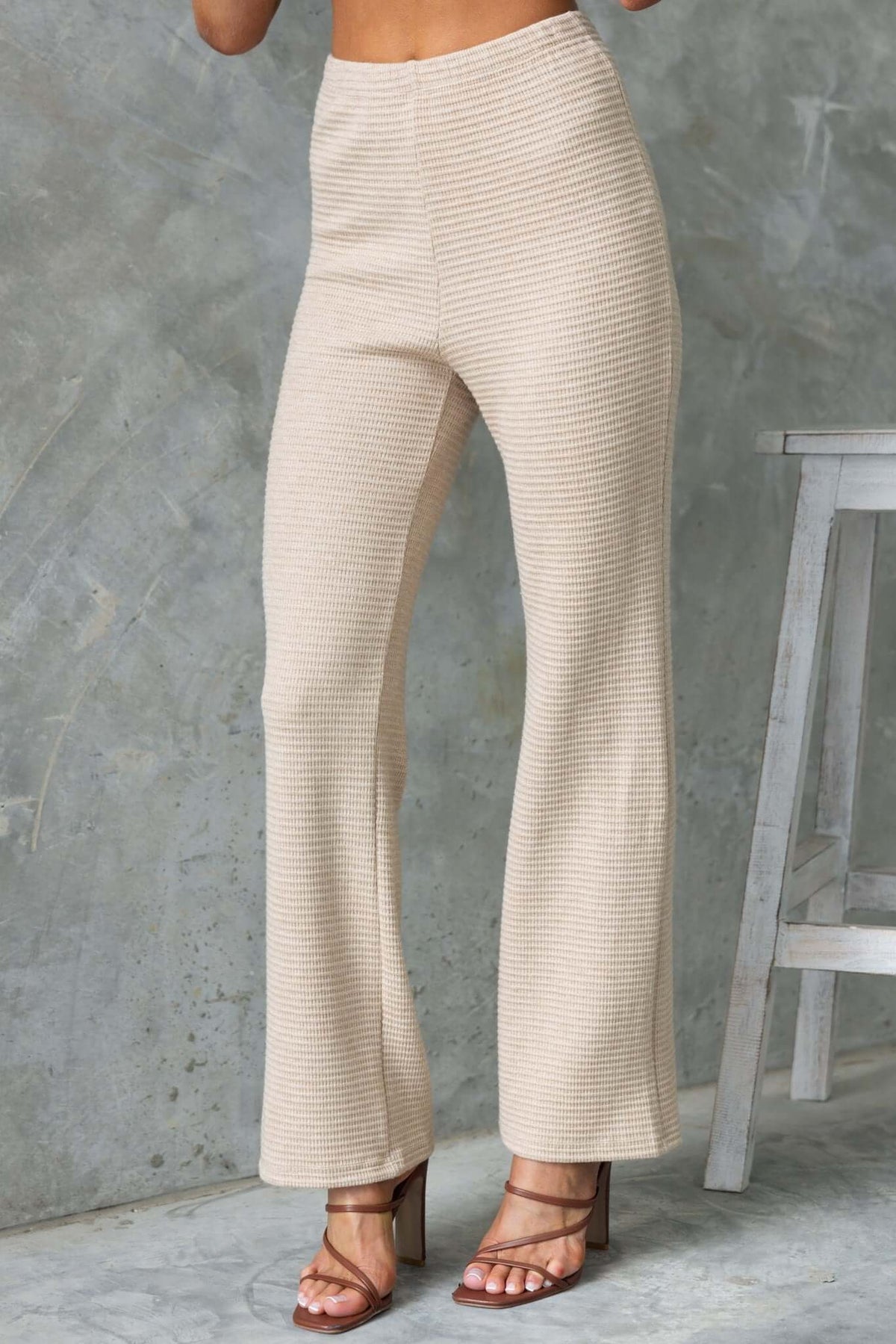 Beige Xandra Pants with mid-high waist, elastic waistband, and drop-crotch style, worn with strappy heels.