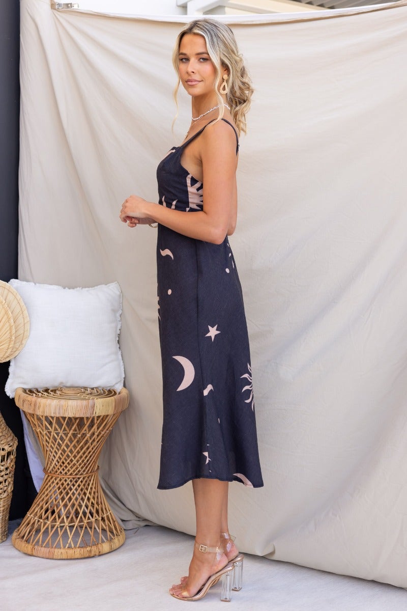 Model wearing a faded black cotton blend midi dress with adjustable straps and celestial print.