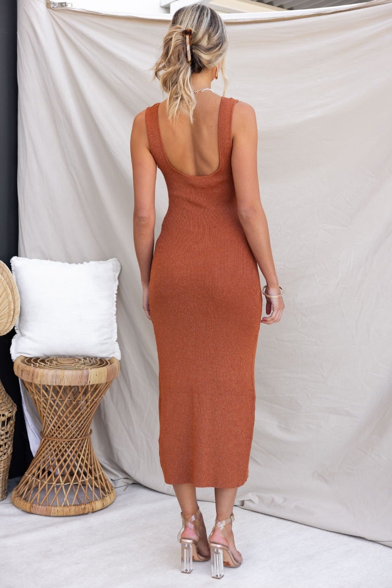 Back view of a ribbed midi dress in burnt orange, featuring a scoop neckline and back cutout, styled with clear heels.