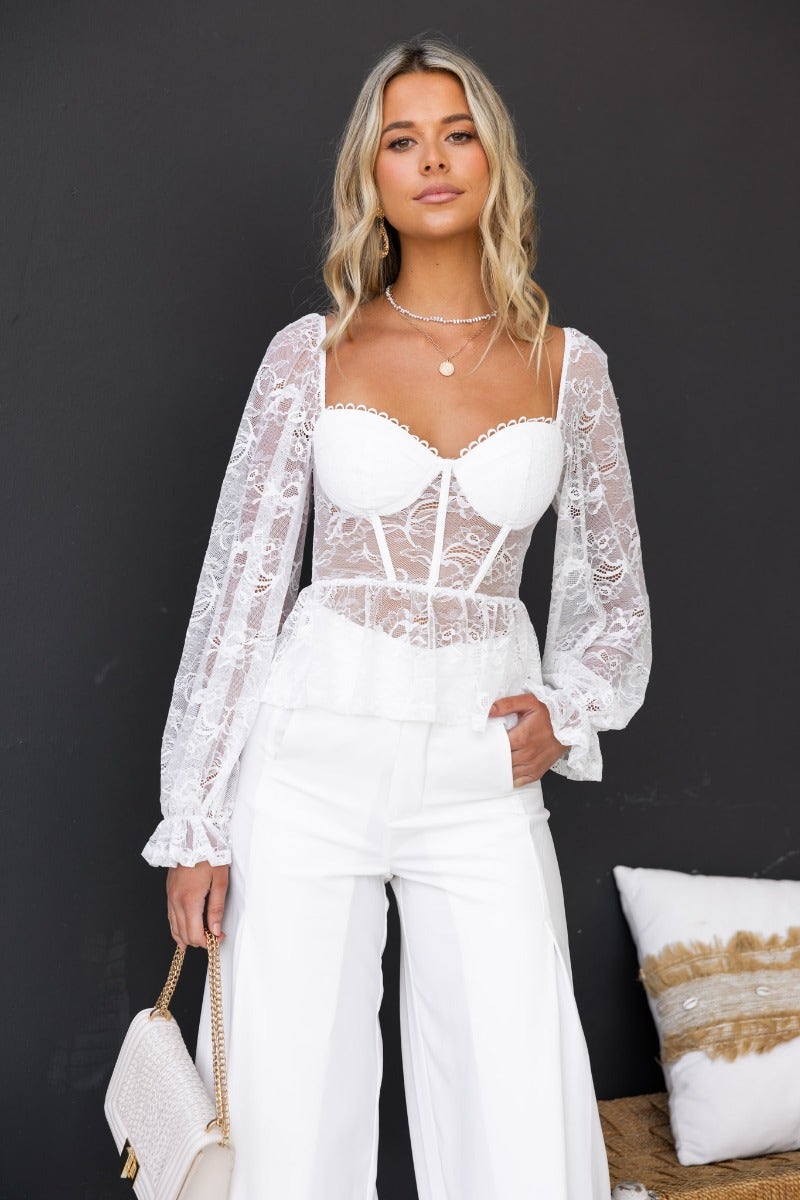 Elegant white lace top with padded bust and long sleeves, styled with wide-leg white pants.